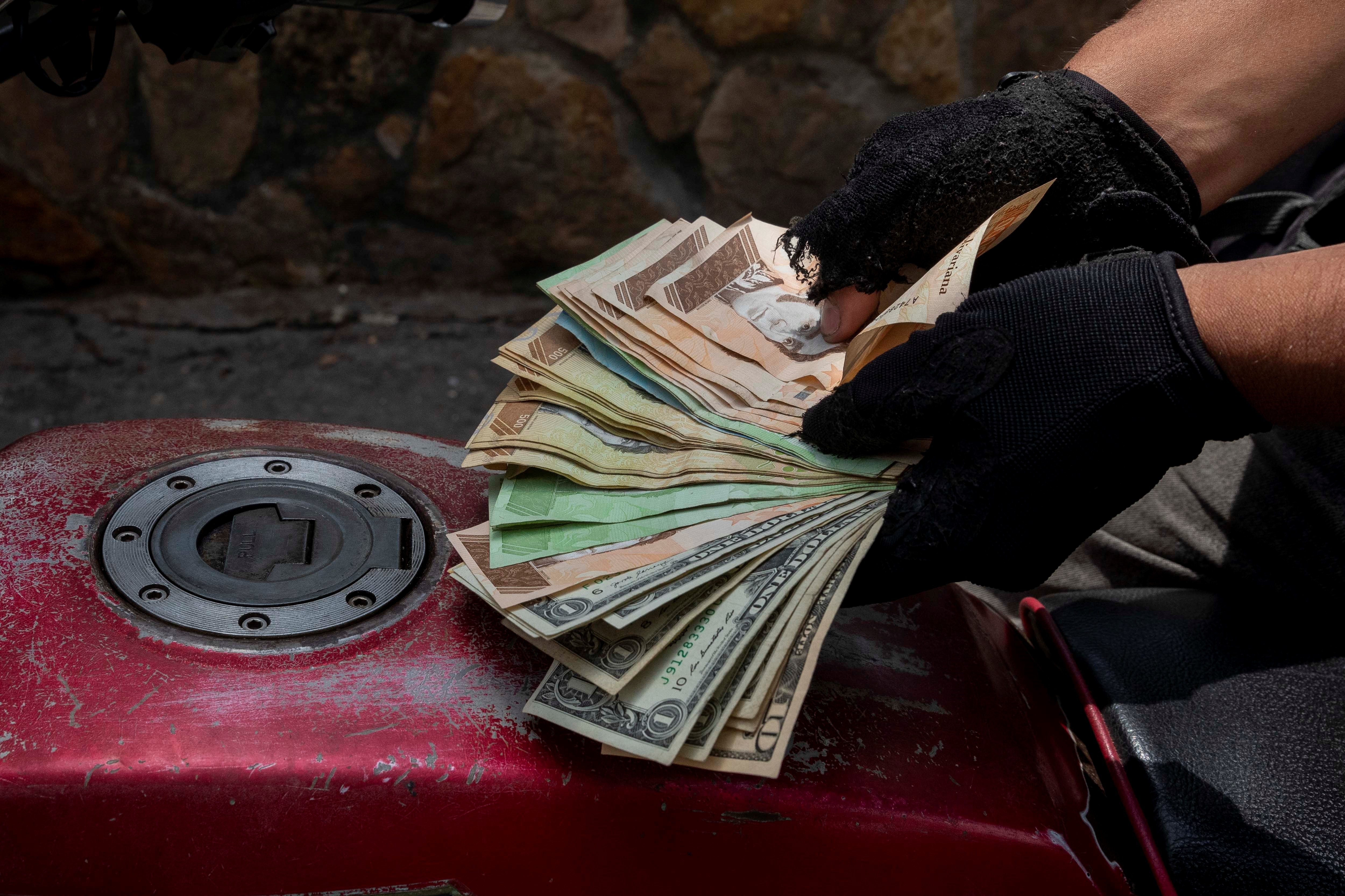 Un hombre muestra este jueves un fajo de bolívares y dólares previo a comprar gasolina para su moto en una estación de servicio, en Caracas (Venezuela). EFE/RAYNER PEÑA R

