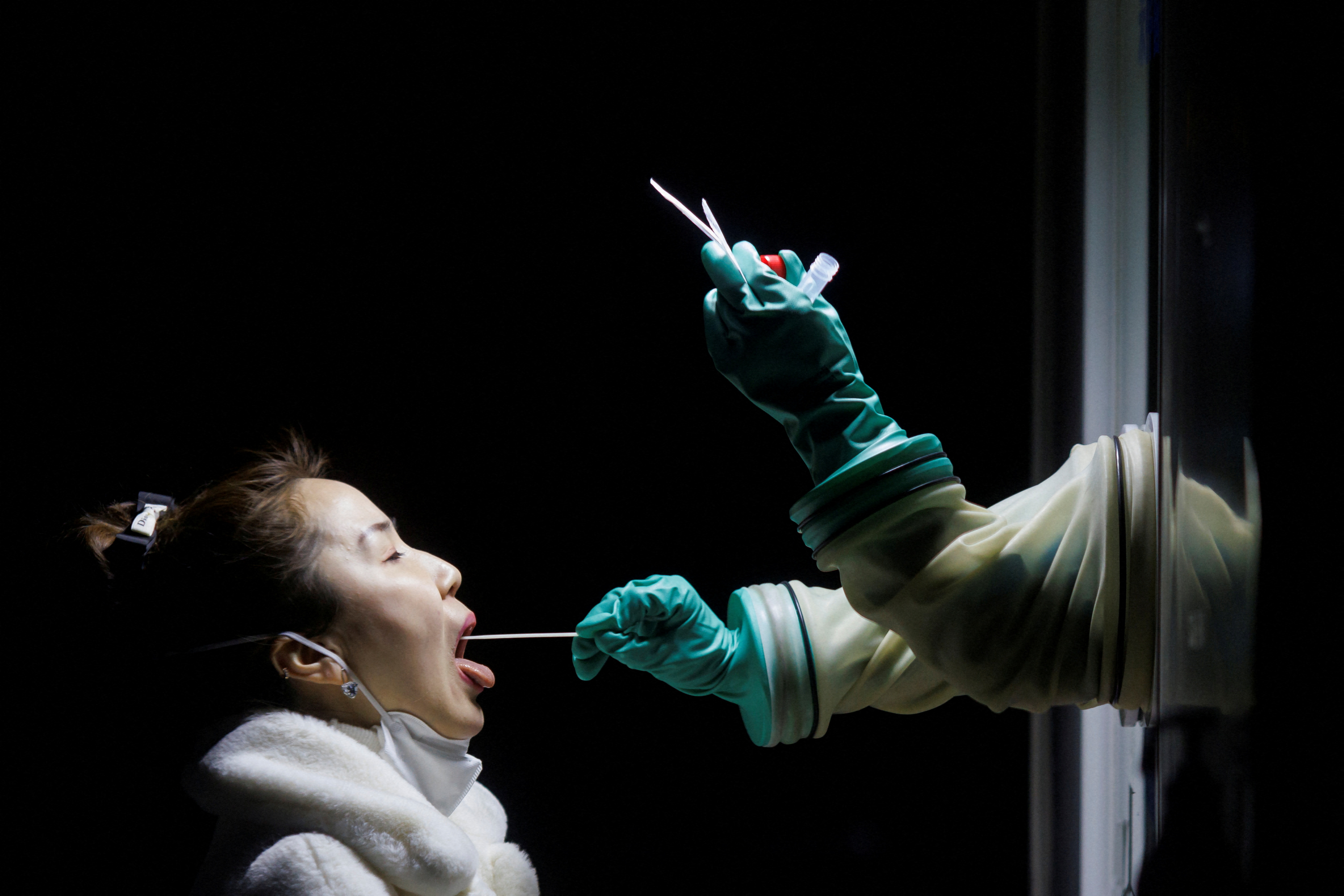A woman receives a throat swab test at a street booth as the coronavirus disease (COVID-19) pandemic continues in Beijing, China, January 17, 2022. REUTERS/Thomas Peter     TPX IMAGES OF THE DAY