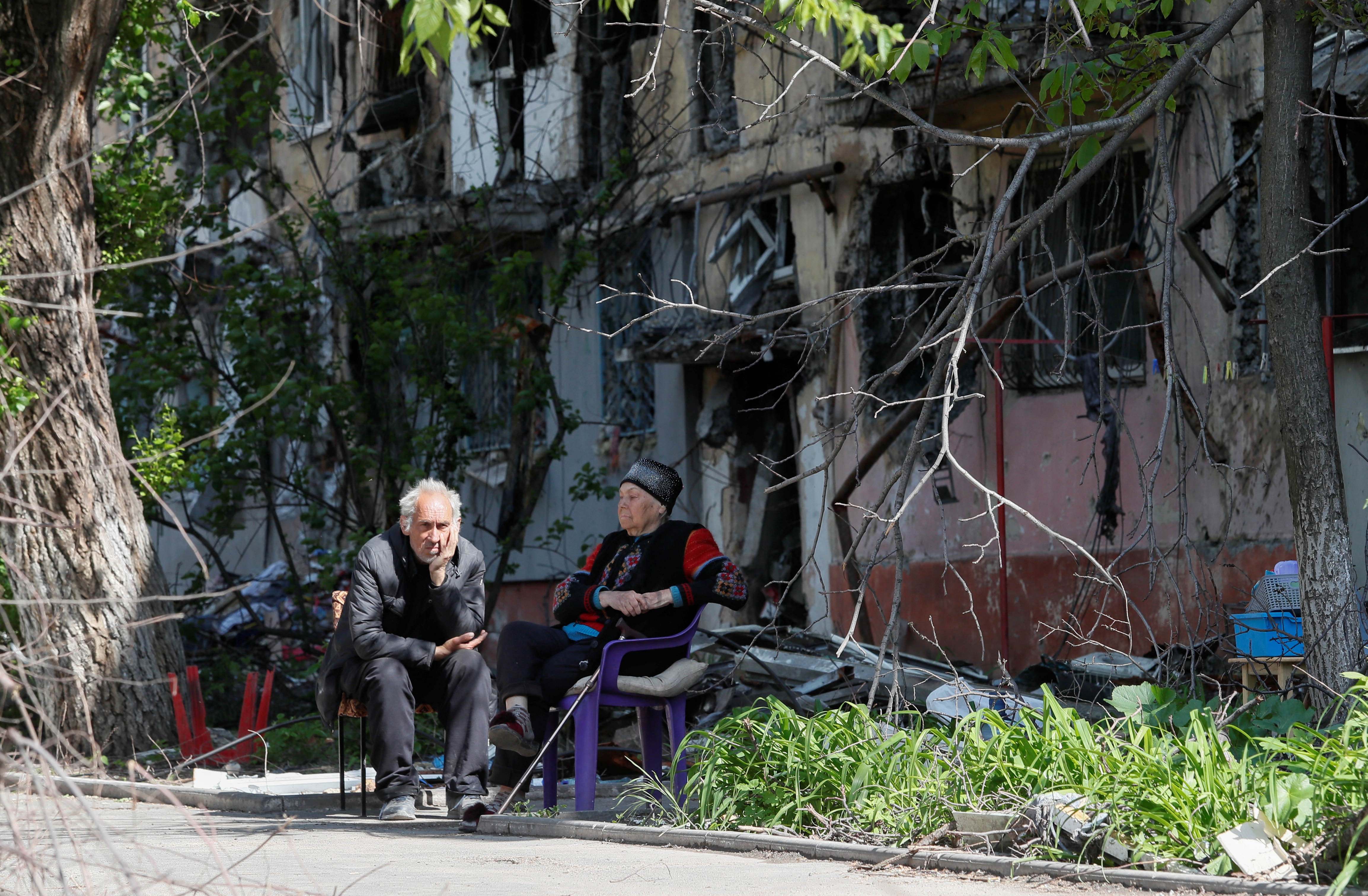 Local residents sit in a courtyard near a block of flats heavily damaged during Ukraine-Russia conflict in the southern port city of Mariupol, Ukraine May 20, 2022. REUTERS/Alexander Ermochenko
