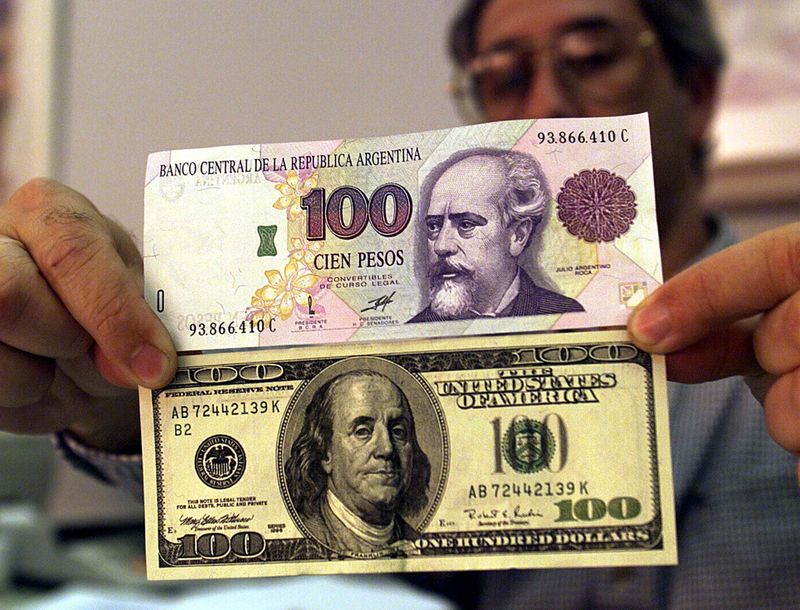 Foto de archivo - Un hombre muestra un billete de 100 pesos argentinos y otro de 100 dólares estadounidenses, en Buenos Aires, en momentos de una notoria depreciación de la moneda doméstica.