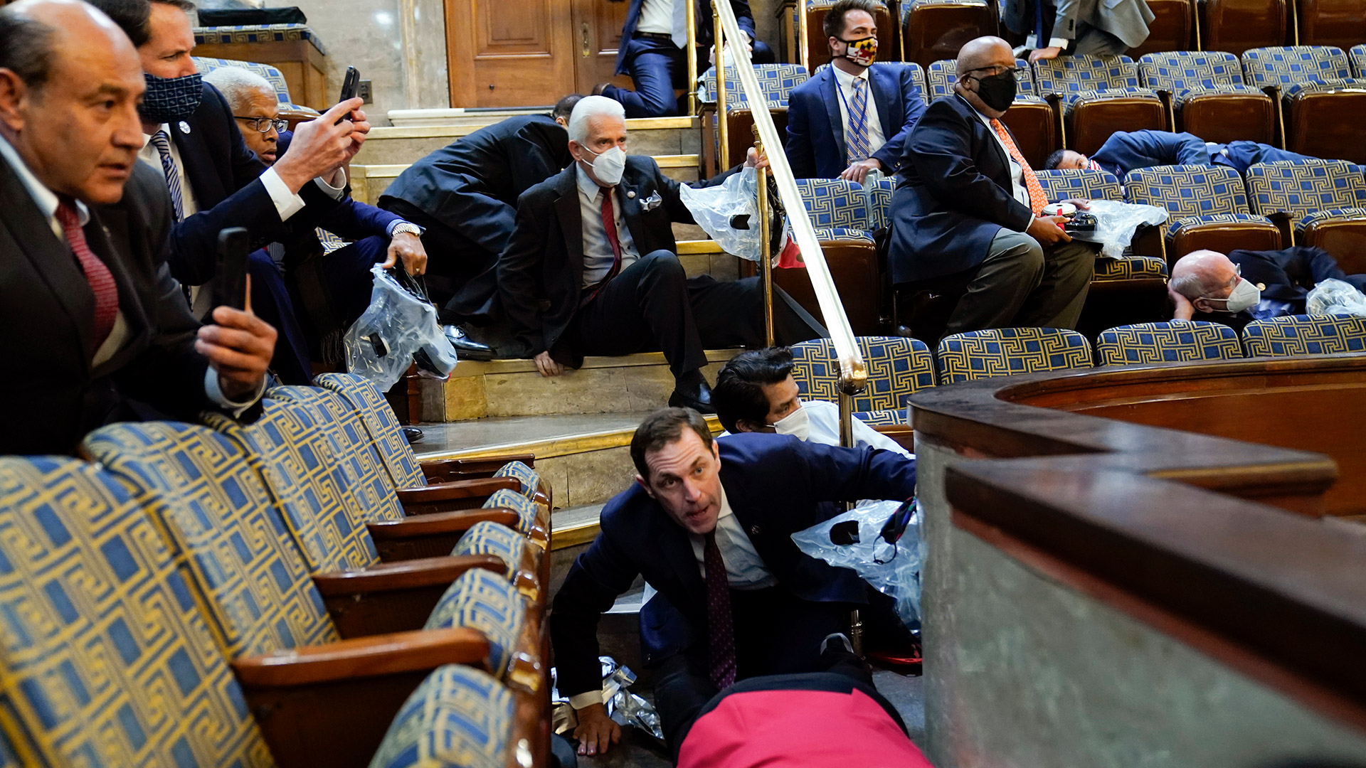 Un grupo de funcionarios del Congreso se refugia en la galería de la Cámara de Representantes mientras los manifestantes tratan de entrar al recinto (Foto AP/Andrew Harnik)