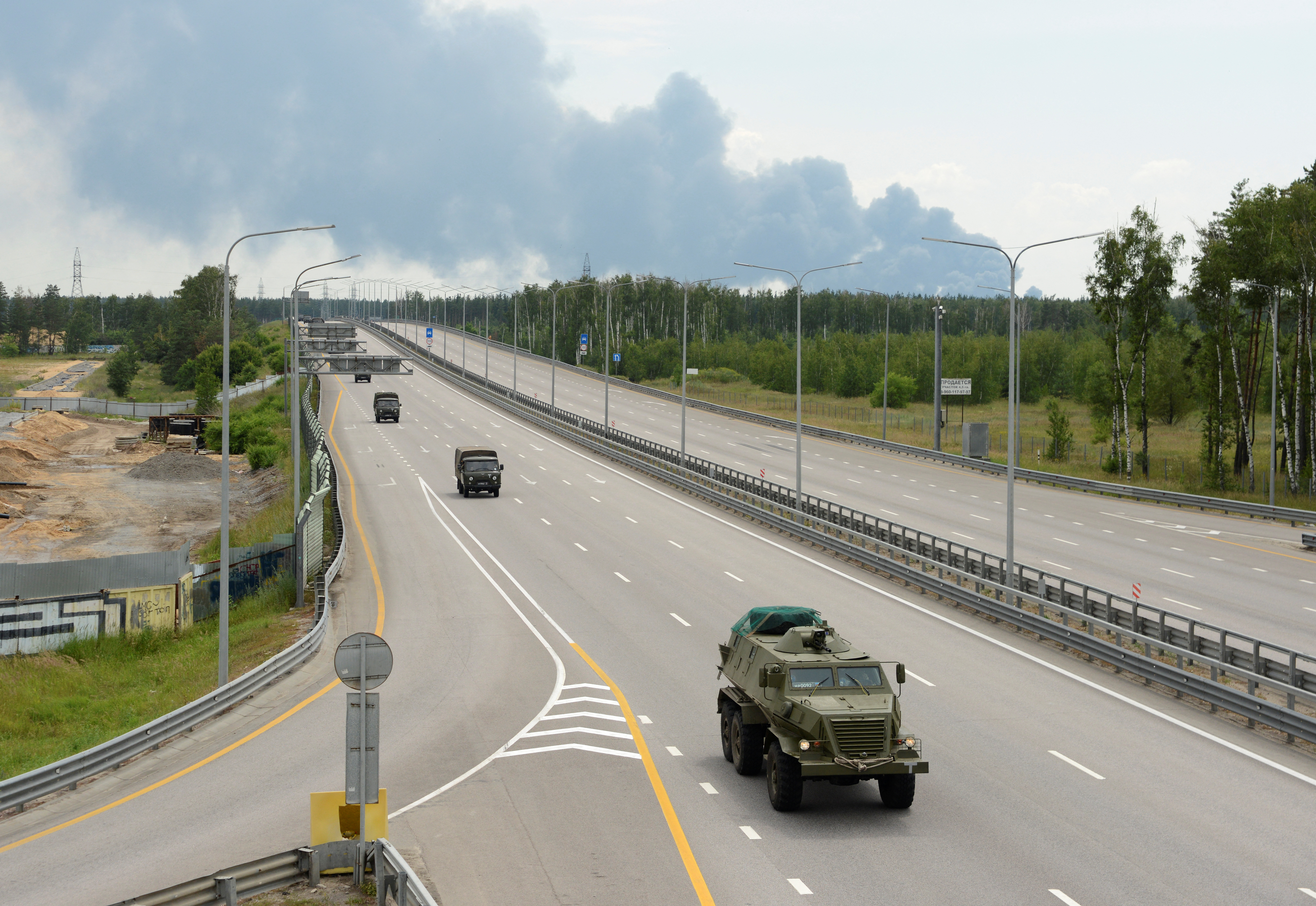 Una columna militar del grupo mercenario privado Wagner circula por la autopista M-4, que une la capital Moscú con las ciudades del sur de Rusia, con el humo de un tanque de combustible en llamas en un depósito de petróleo visto en el fondo, cerca de Voronezh, Rusia, 24 de junio de 2023. REUTERS/Stringer