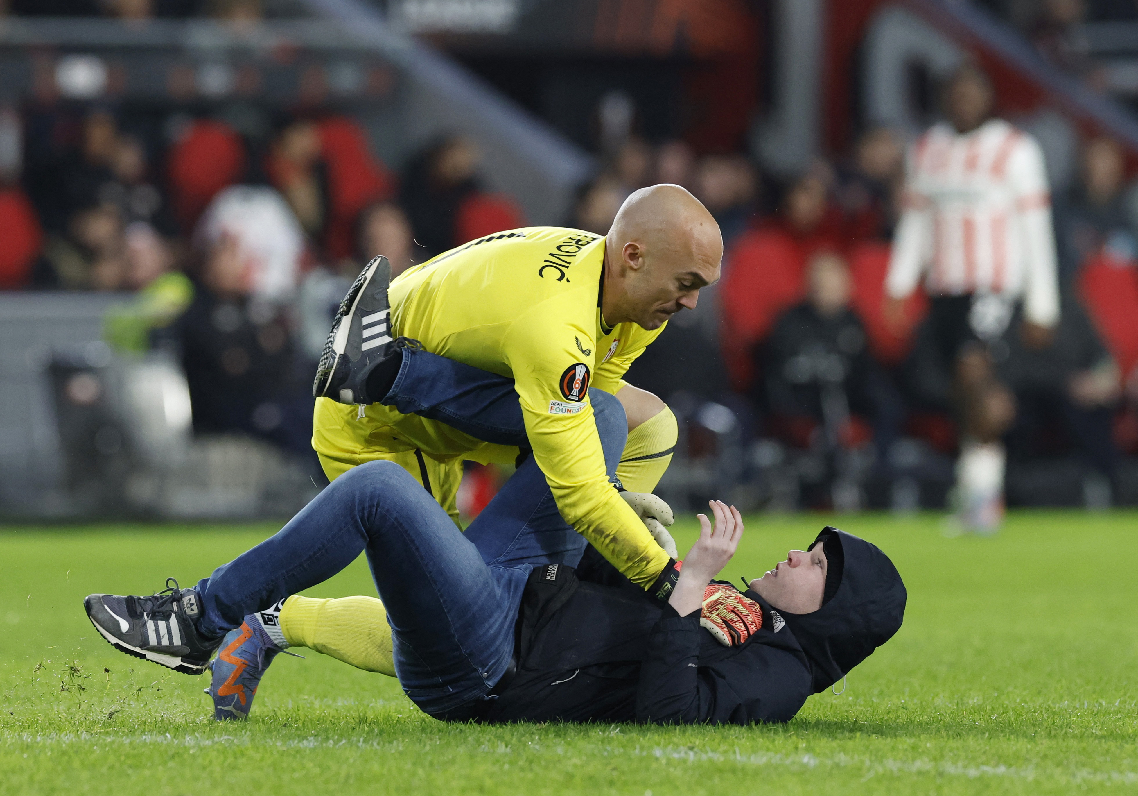 El arquero Marko Dmitrovic tumba al agresor y lo retiene en el suelo durante el partido entre Sevilla y PSV en Eindhoven (REUTERS/Piroschka Van De Wouw)