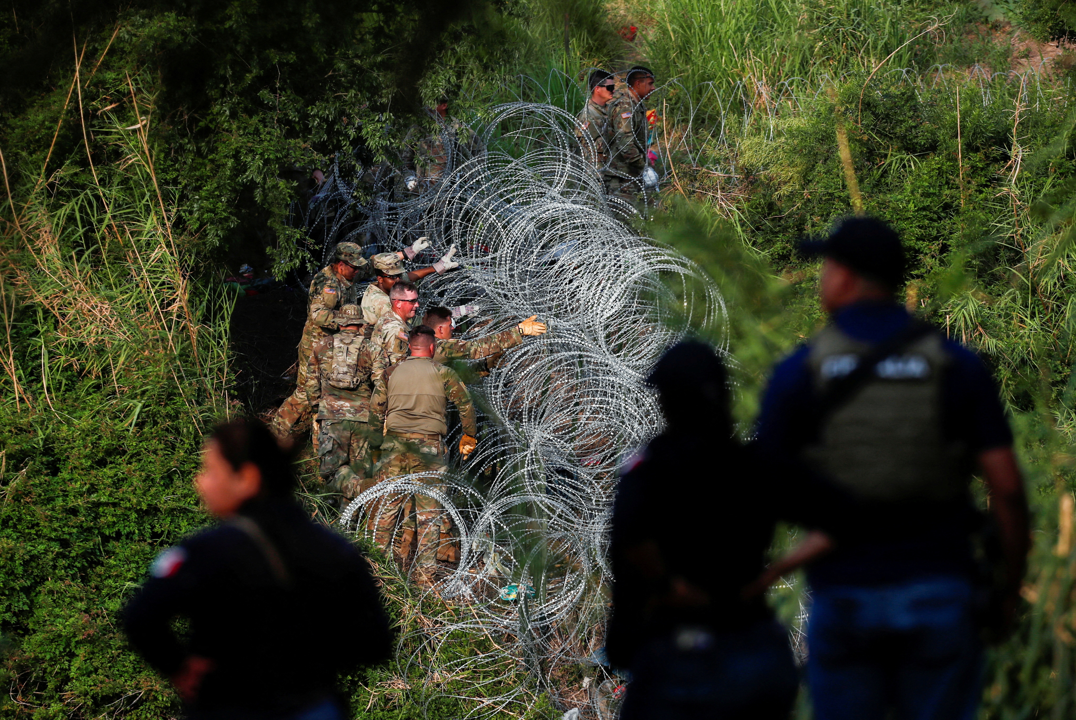 Soldados de la Guardia Nacional de Texas colocan más alambre de púas en las orillas del río Bravo mientras los solicitantes de asilo cruzan la frontera para entregarse a los agentes de la Patrulla Fronteriza  (REUTERS/Daniel Becerril)