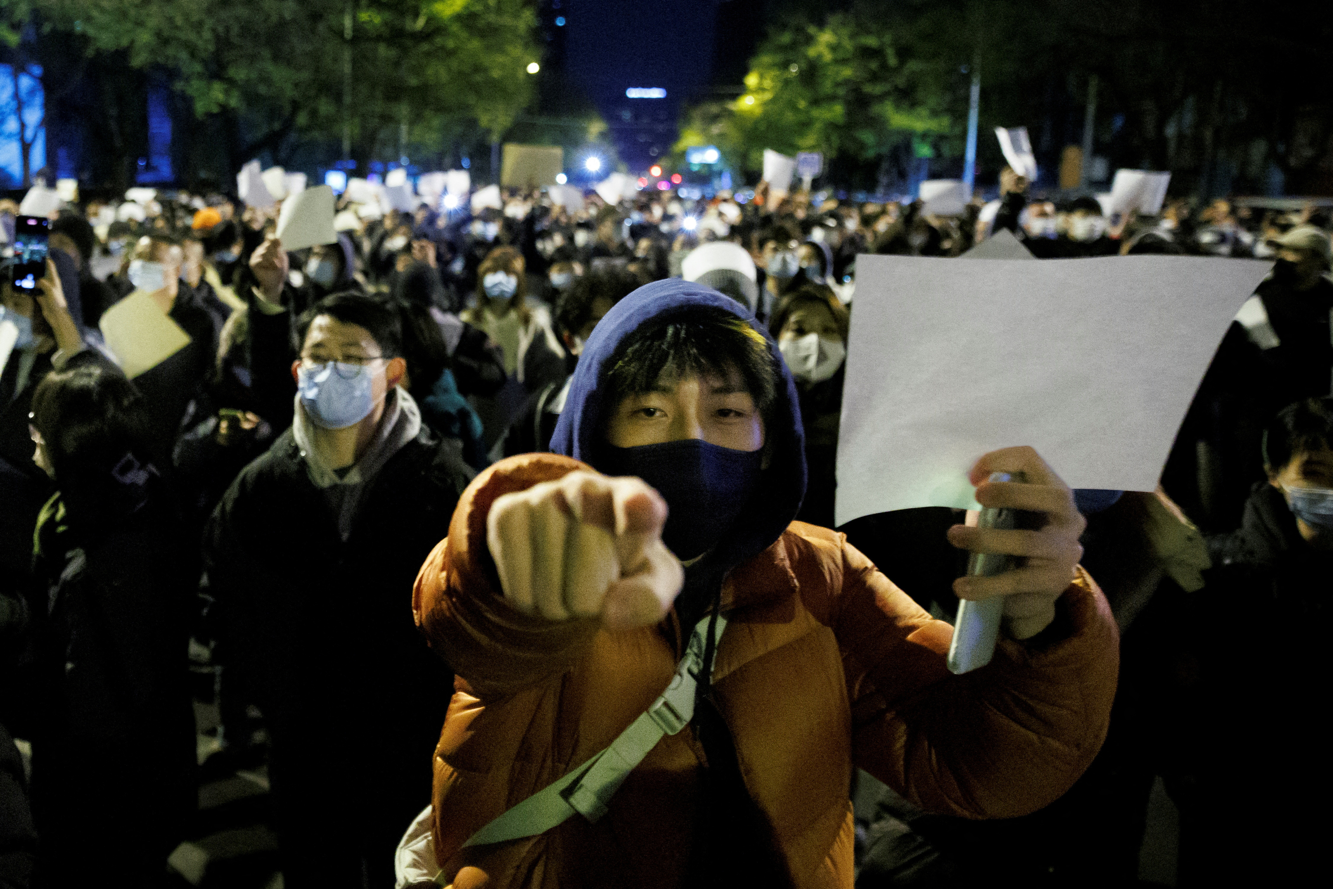 Personas sostienen hojas de papel blancas en protesta por las restricciones de la enfermedad por coronavirus (COVID-19), después de una vigilia por las víctimas de un incendio en Urumqi, mientras continúan los brotes de COVID-19, en Beijing