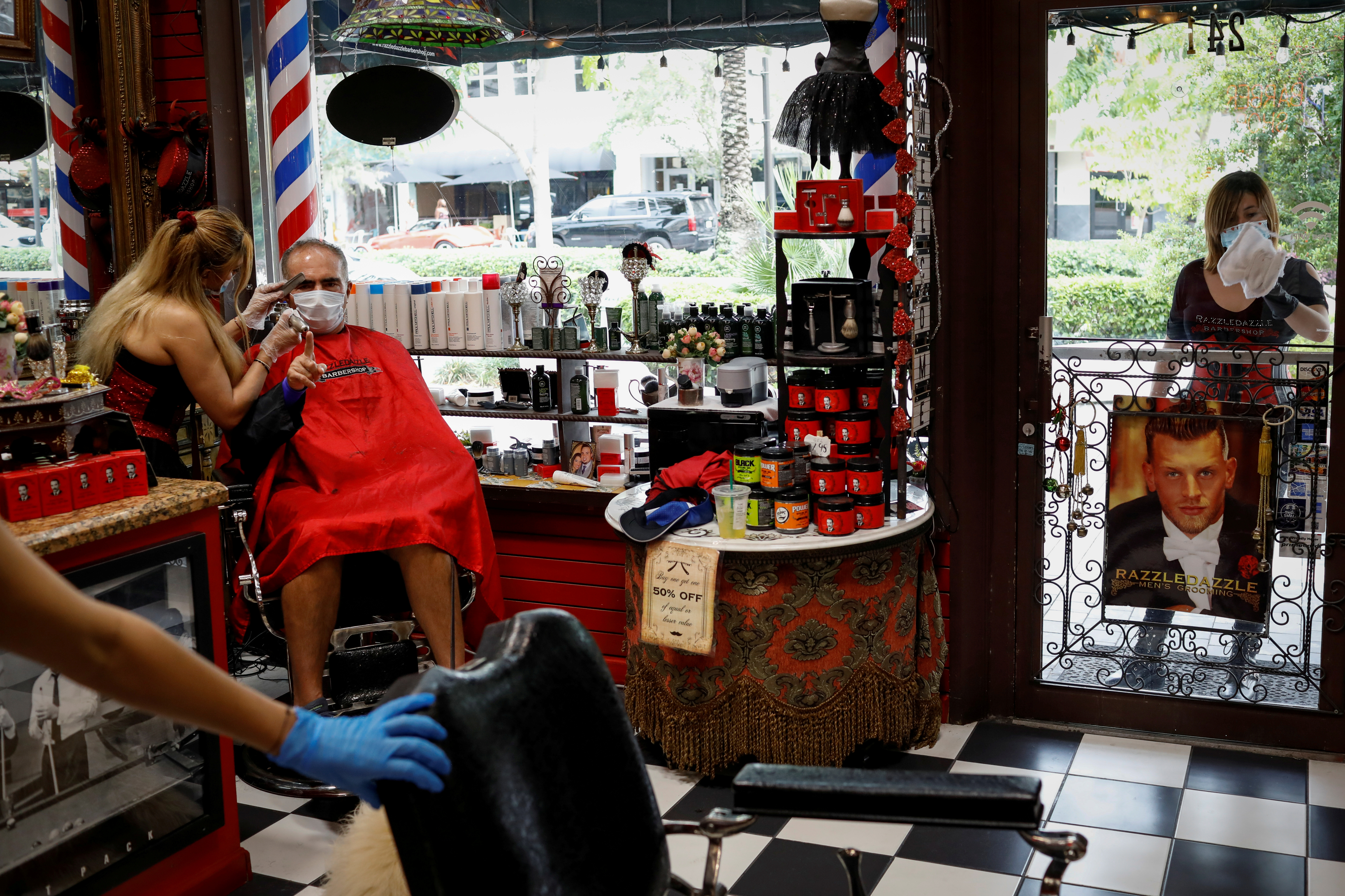  Un peluquero con una máscara protectora corta el pelo de un hombre en una peluquería de Miami