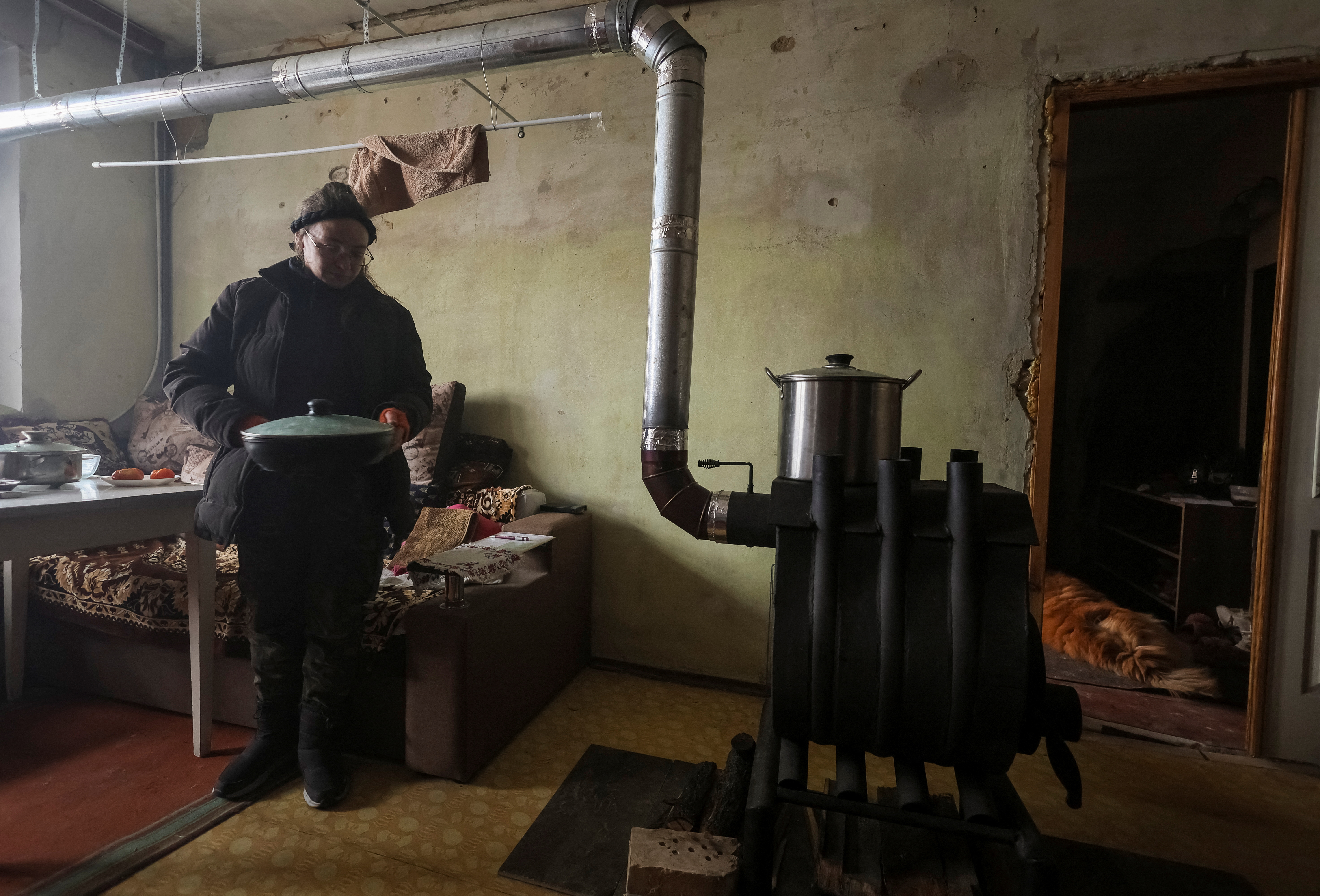La residente local Tetiana Reznychenko, de 43 años, prepara comida en una estufa de leña instalada en su apartamento, que no tiene electricidad, calefacción ni agua, en el quinto piso de un edificio de apartamentos destruido por un ataque militar ruso en la aldea ucraniana de Horenka, que fue gravemente dañada por los combates en los primeros días de la invasión rusa, 19 de noviembre de 2022. REUTERS/Gleb Garanich
