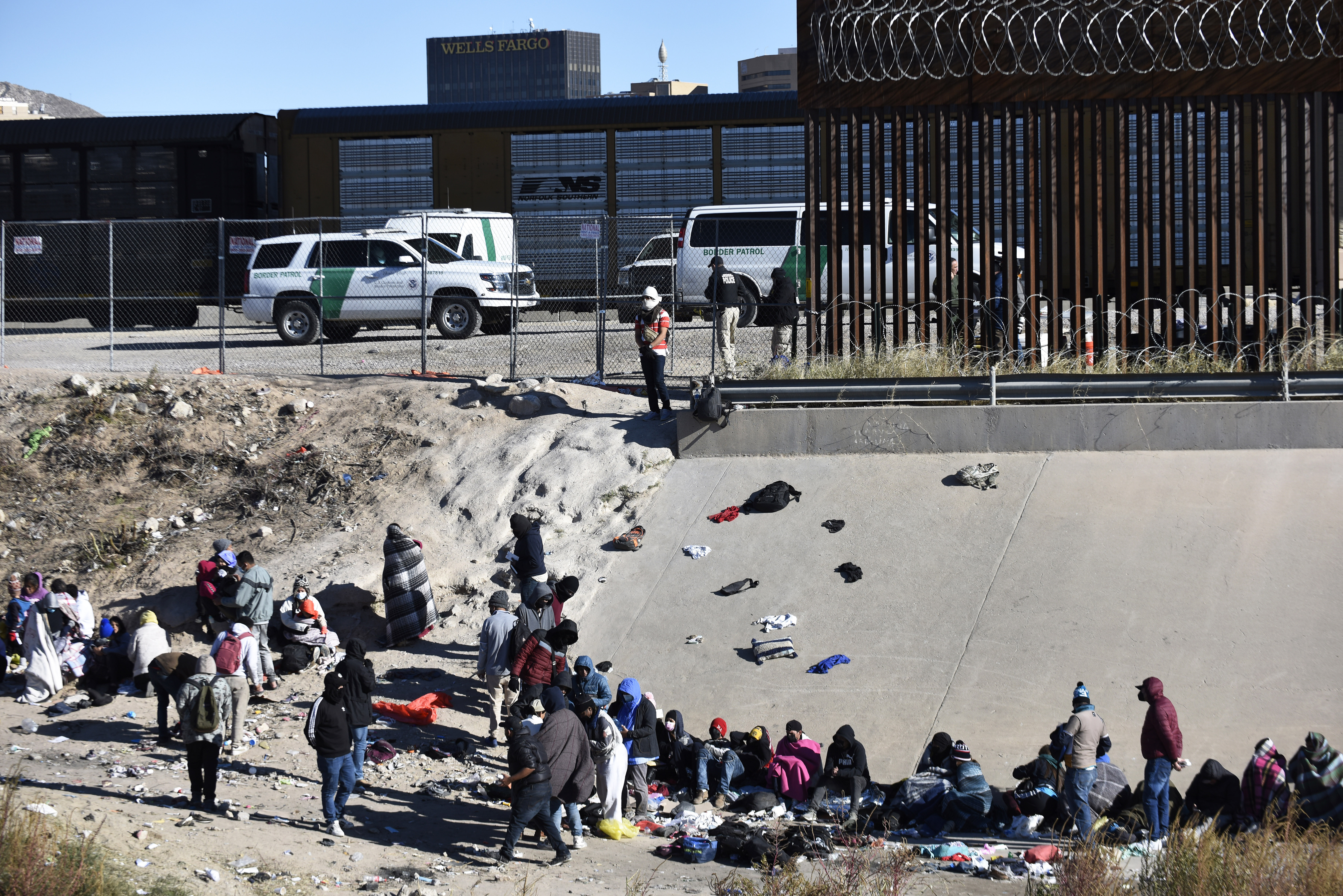 Migrantes esperan a cruzar la frontera entre Estados Unidos y México, el miércoles 14 de diciembre de 2022, desde Ciudad Juárez, México, frente a vehículos de la Patrulla Fronteriza en El Paso, Texas  (AP/Christian Chávez)