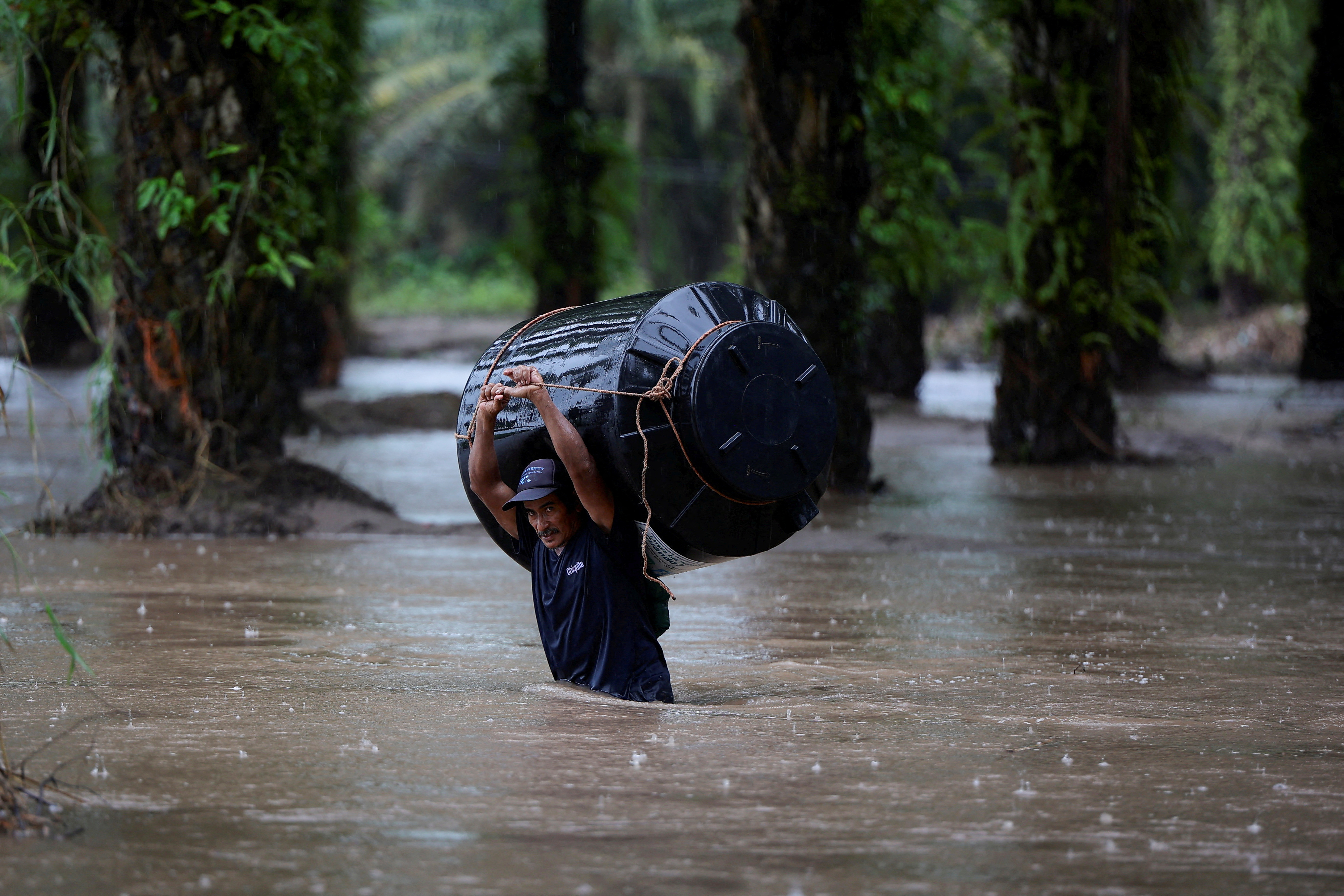 Un hombre lleva un tanque de agua vacío a través de un área inundada después del impacto este mes de la tormenta tropical Julia, en Honduras (REUTERS/Yoseph Amaya)