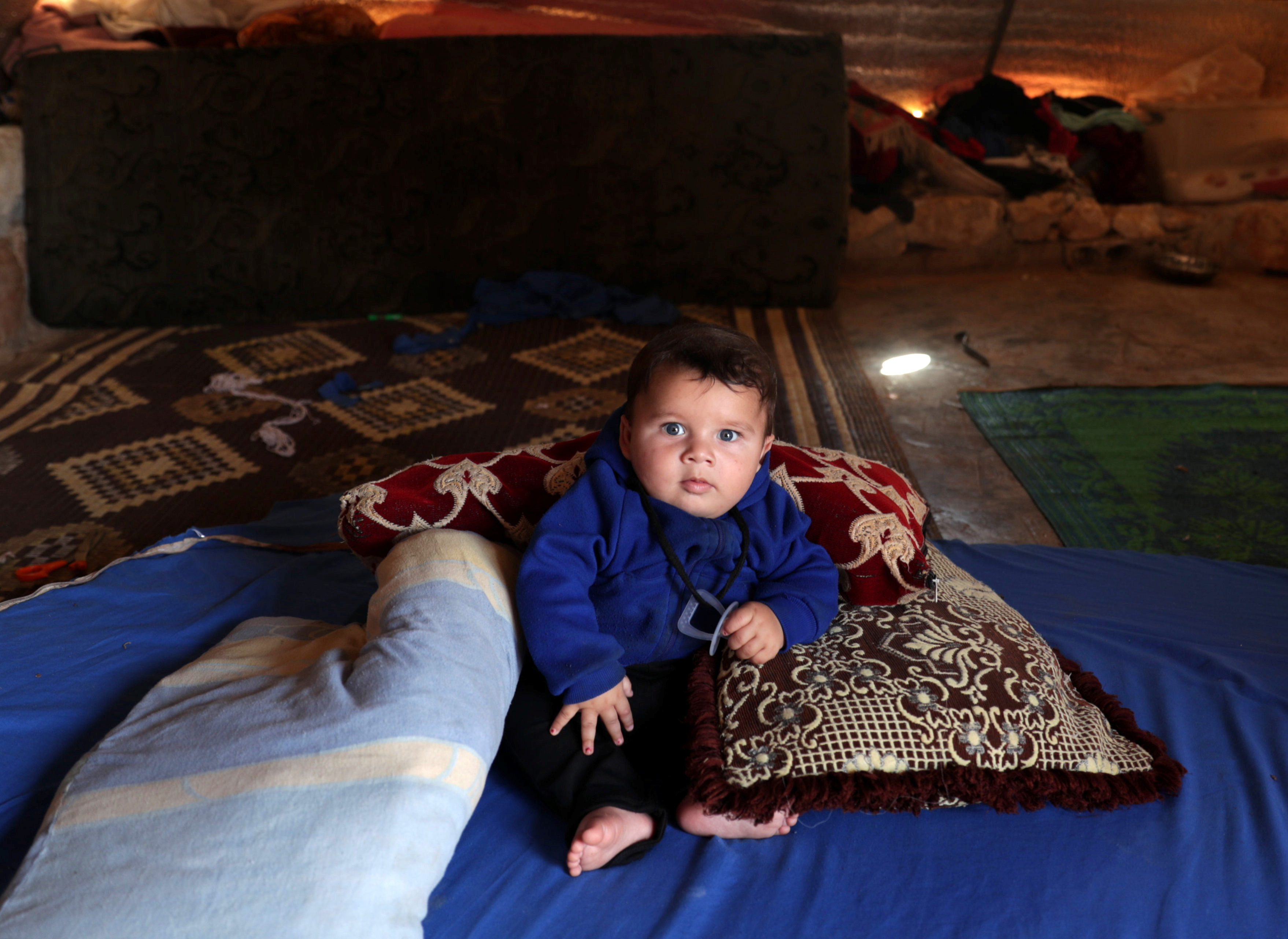 Abdul Rahman al-Fares, un bebé de 4 meses apoyado sobre almohadas sobre una manta azul en la tienda de su familia. El sábado fue el el Día Mundial de los Refugiados, que fue el sábado. (REUTERS/Khalil Ashawi)