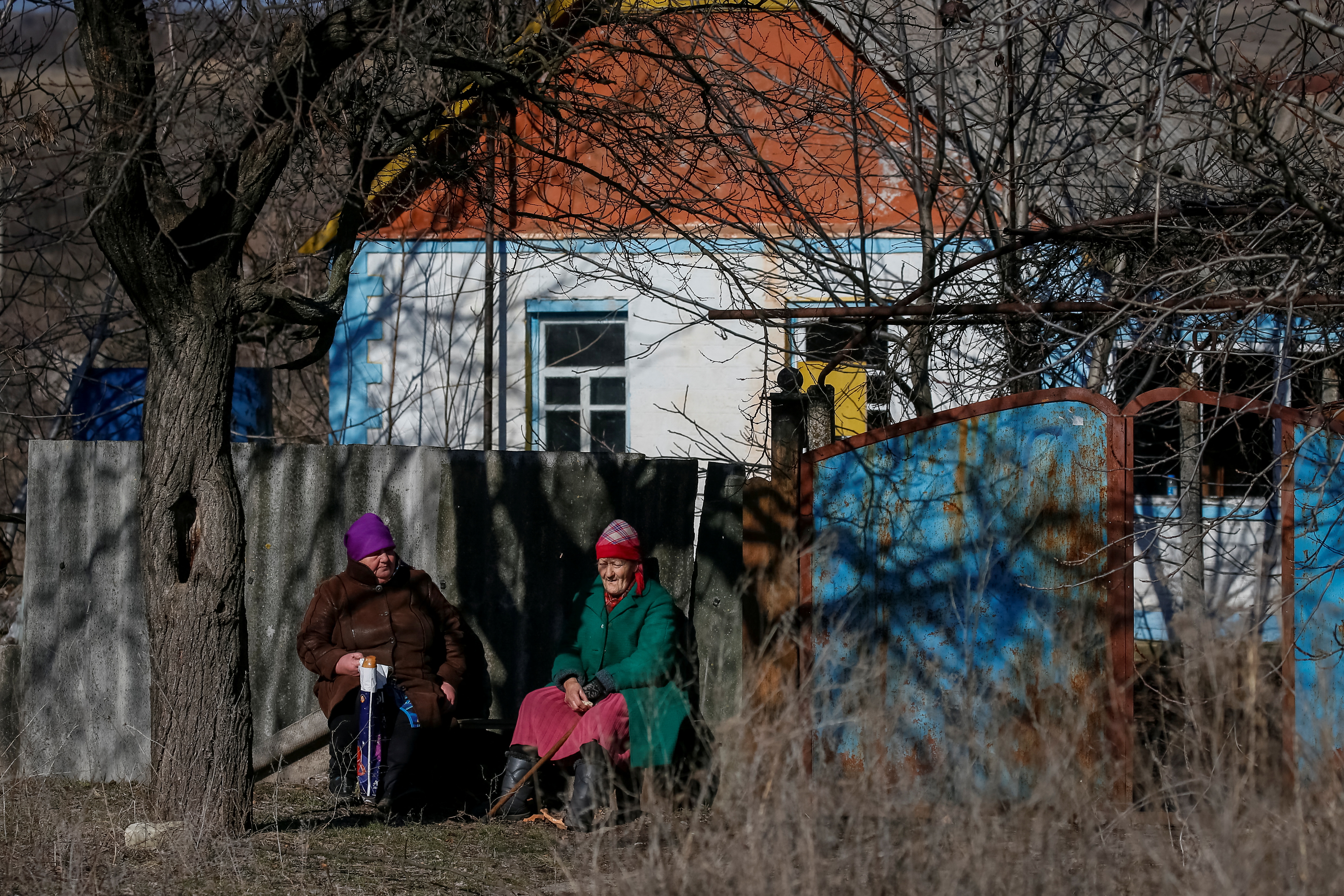 Los residentes locales se sientan frente a una casa cerca de la línea del frente en el pueblo de Travneve en la región de Donetsk, Ucrania, el 21 de febrero de 2022 (REUTERS/Gleb Garanich)