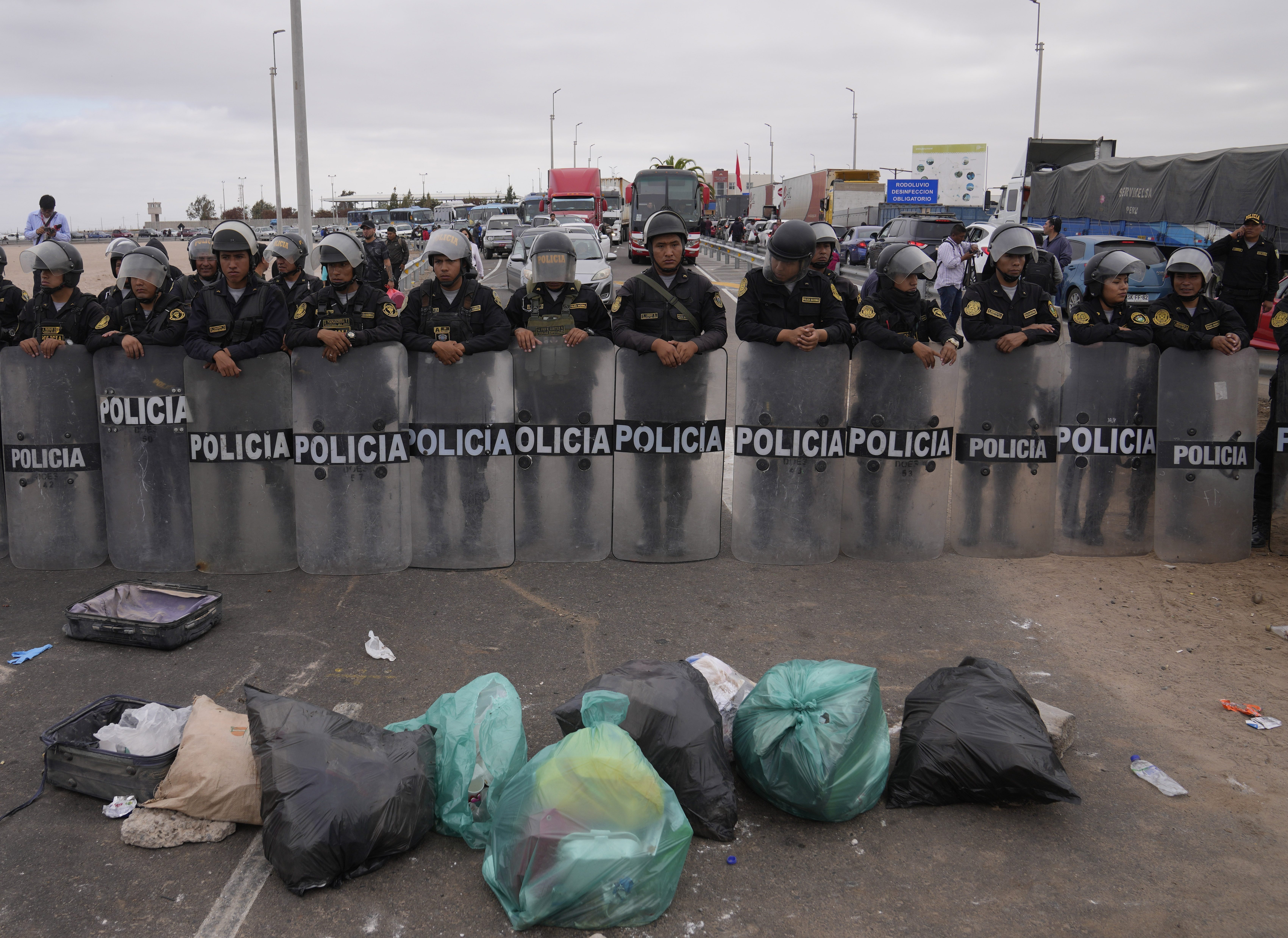 Venezuelan migrants block entry to Chile with garbage in front of a Peruvian riot police barricade on the Peruvian border with Chile, in Tacna, Peru, Saturday, April 29, 2023. A migration crisis on the Chile-Peru border has intensified as hundreds of migrants were stranded unable to cross into Peru.  (AP Photo/Martin Mejia)