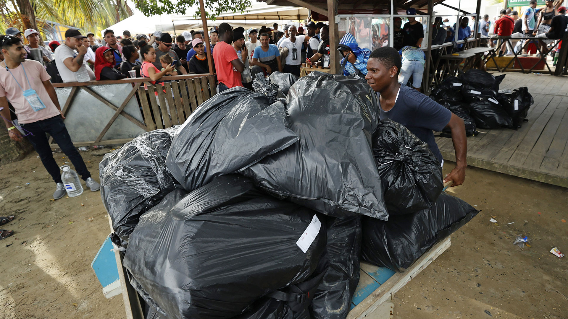 Un joven lleva maletas envueltas en bolsas plásticas hacia un embarcadero (EFE/Mauricio Dueñas Castañeda)