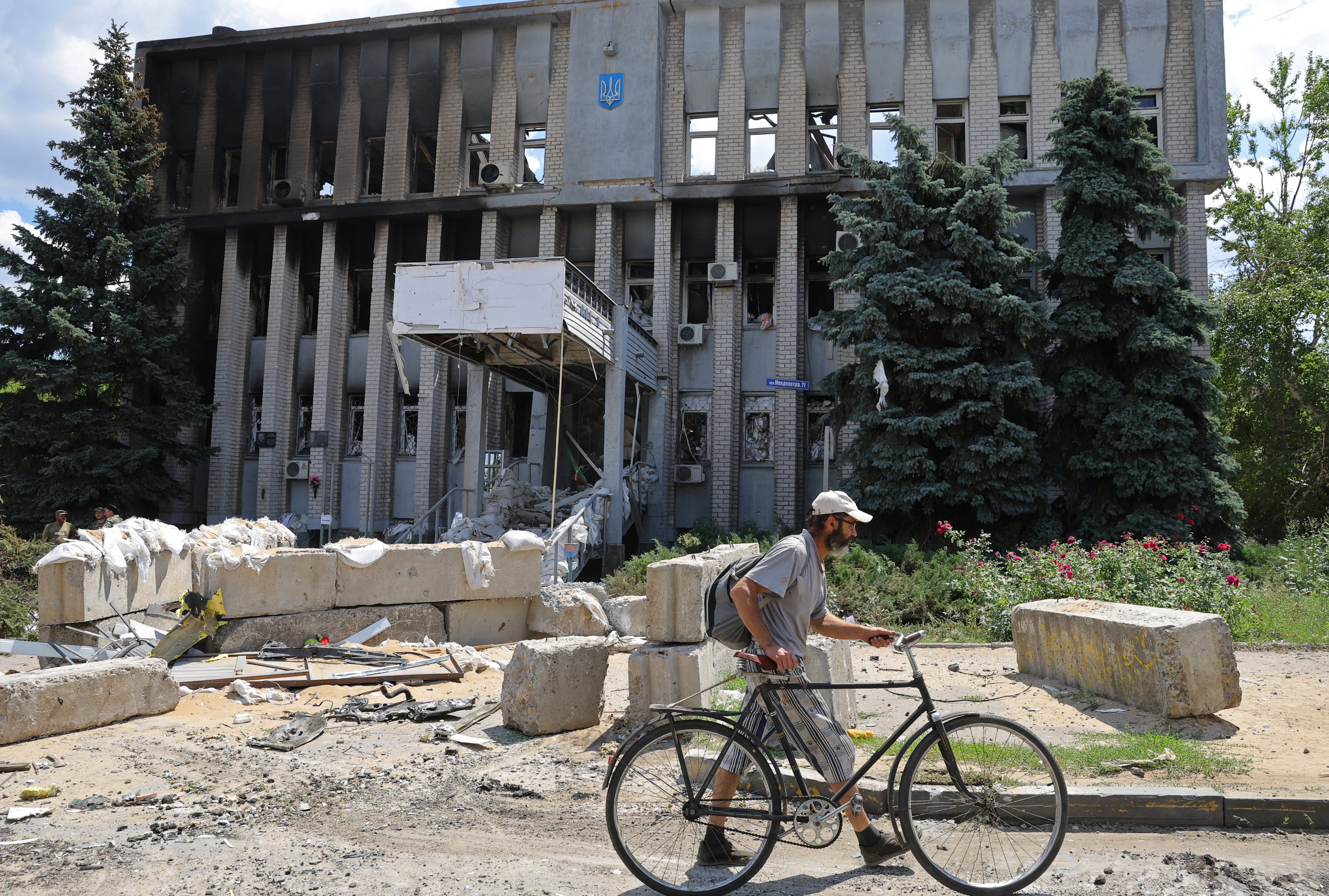 Un residente local camina con una bicicleta frente a un edificio destruido del departamento de policía durante la sangrienta invasión rusa a Ucrania en la ciudad de Lysychansk en la región de Luhansk, Ucrania este 4 de julio de 2022 (Reuters)