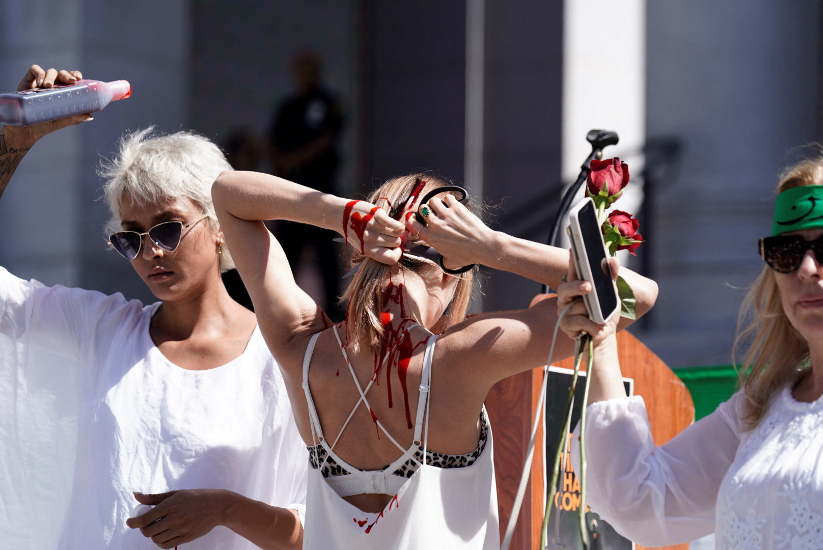 La activista bielorrusa Yadviga Krasovskaya se corta el pelo mientras la artista y activista iraní-estadounidense Samy Rose Moshiri se prepara para empaparse de sangre falsa en una concentración por la libertad de Irán, en protesta por el apoyo a las mujeres iraníes y contra la muerte de Mahsa Amini, frente al Ayuntamiento de Los Ángeles, California, Estados Unidos, 1 de octubre de 2022.  REUTERS/Bing Guan
