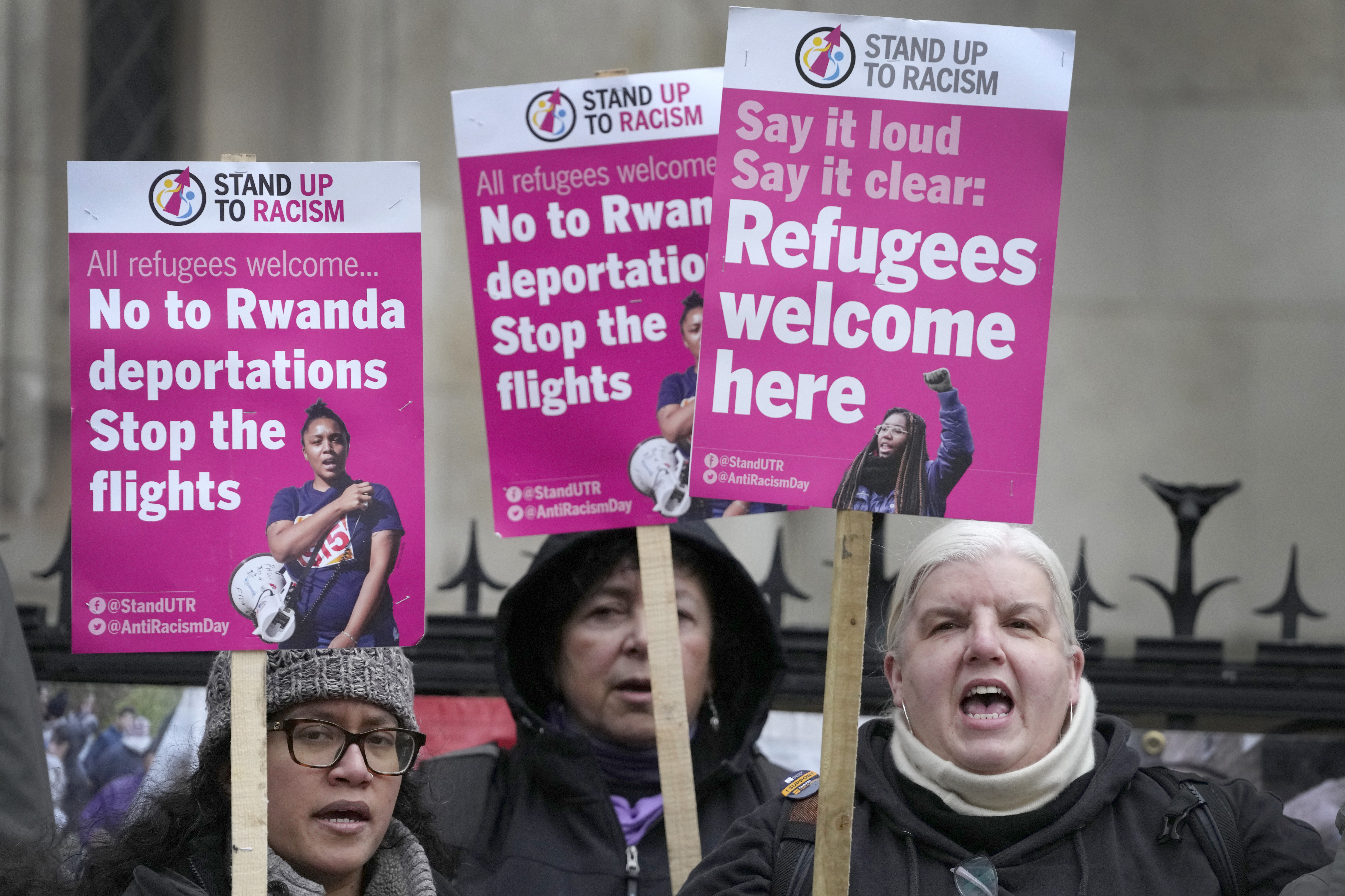 Activistas del grupo Stand Up To Racism sostienen carteles ante el Alto Tribunal de Londres el lunes 19 de diciembre de 2022. El controvertido plan del gobierno británico de enviar a solicitantes de asilo a Ruanda en un viaje sólo de ida es legal, según concluyeron el lunes los jueces del Alto Tribunal británico. (AP Foto/Kirsty Wigglesworth)