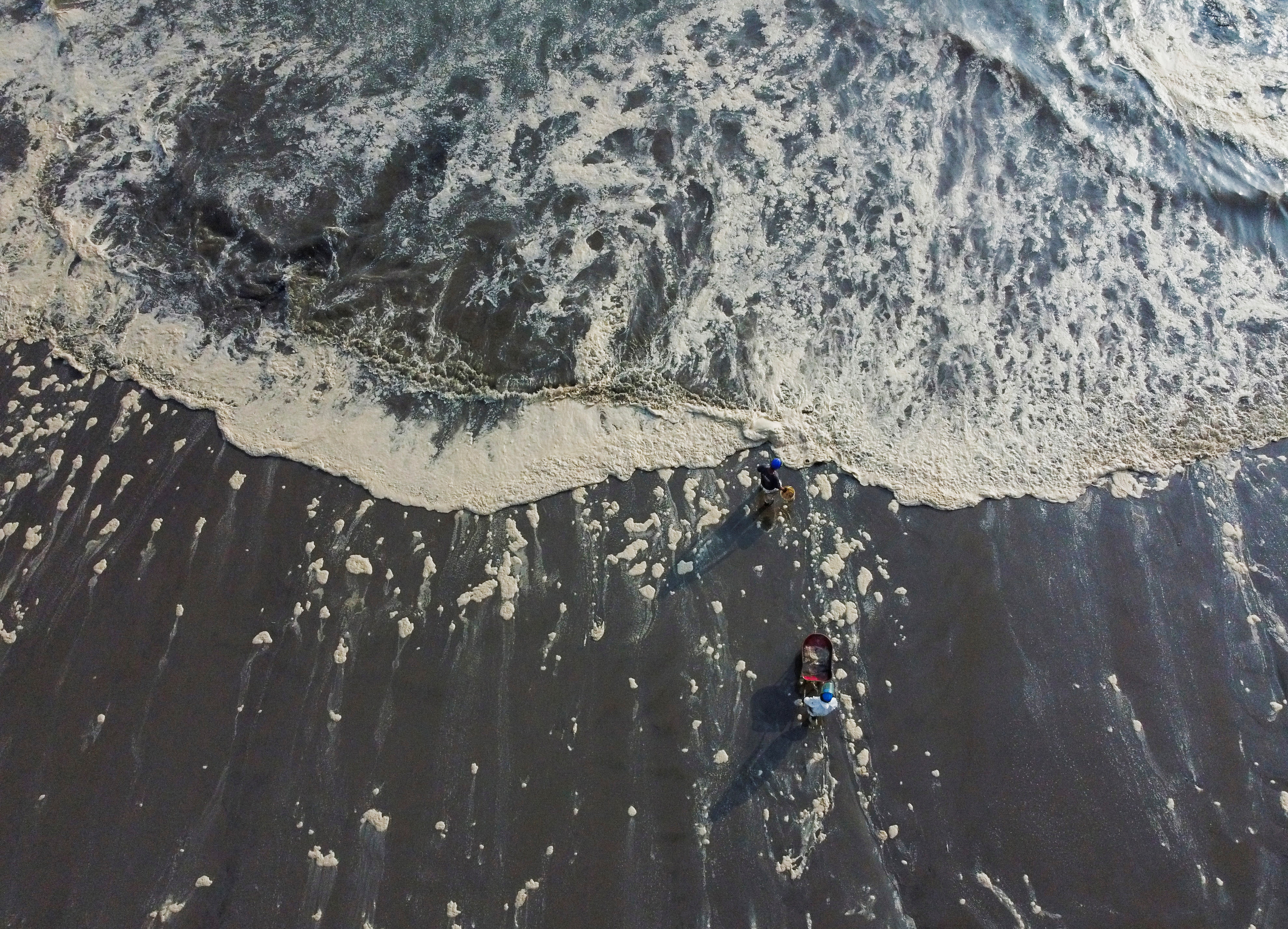 Workers walk through foam on a shore affected by an oil spill caused by abnormal waves, triggered by a massive underwater volcanic eruption in Tonga, off the coast of Lima, in Ventanilla, Peru, January 19, 2022. Picture taken with a drone. REUTERS/Angela Ponce