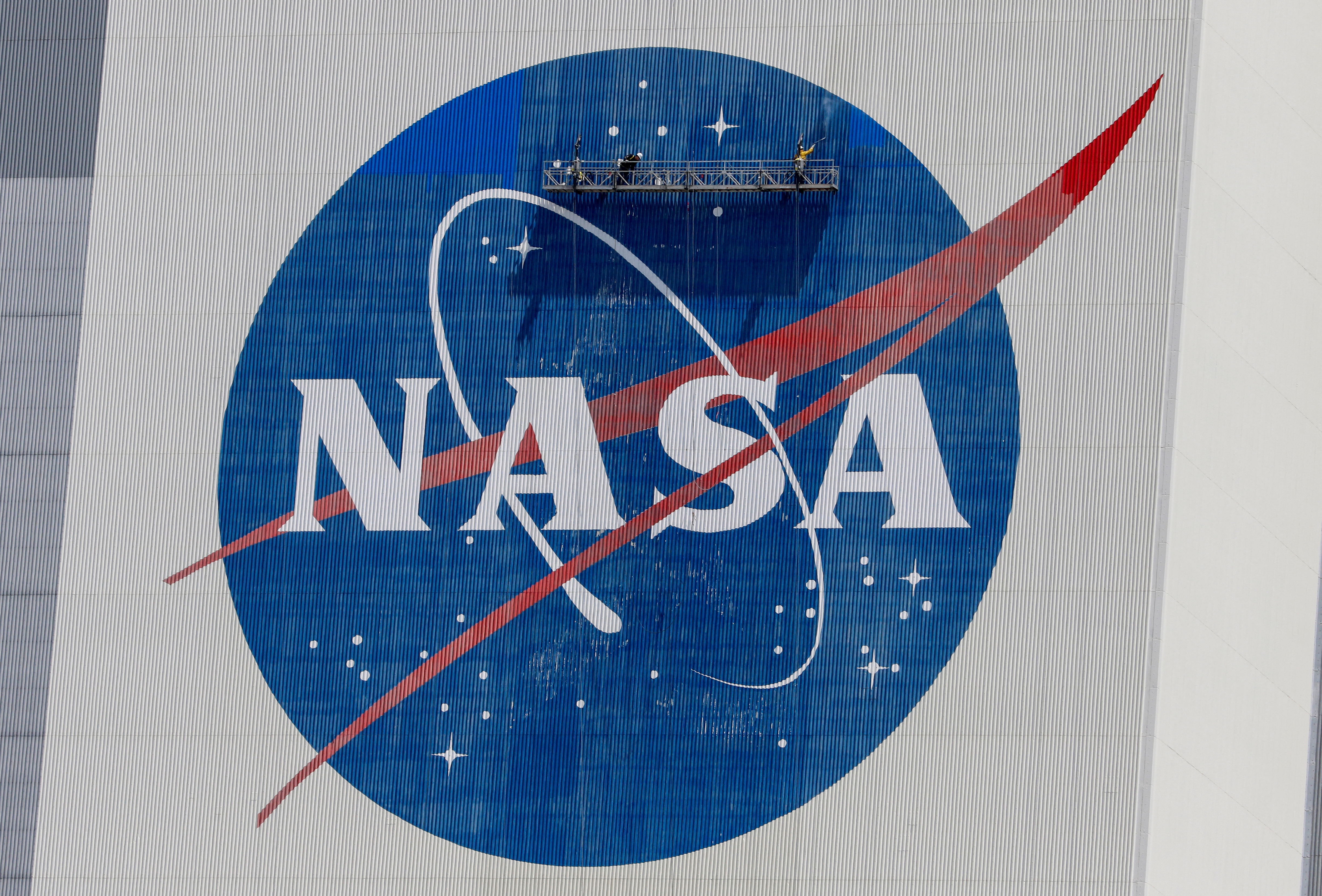 FILE PHOTO: Workers pressure wash the logo of NASA on the Vehicle Assembly Building before SpaceX will send two NASA astronauts to the International Space Station aboard its Falcon 9 rocket, at the Kennedy Space Center in Cape Canaveral, Florida, U.S., May 19, 2020. REUTERS/Joe Skipper/File Photo