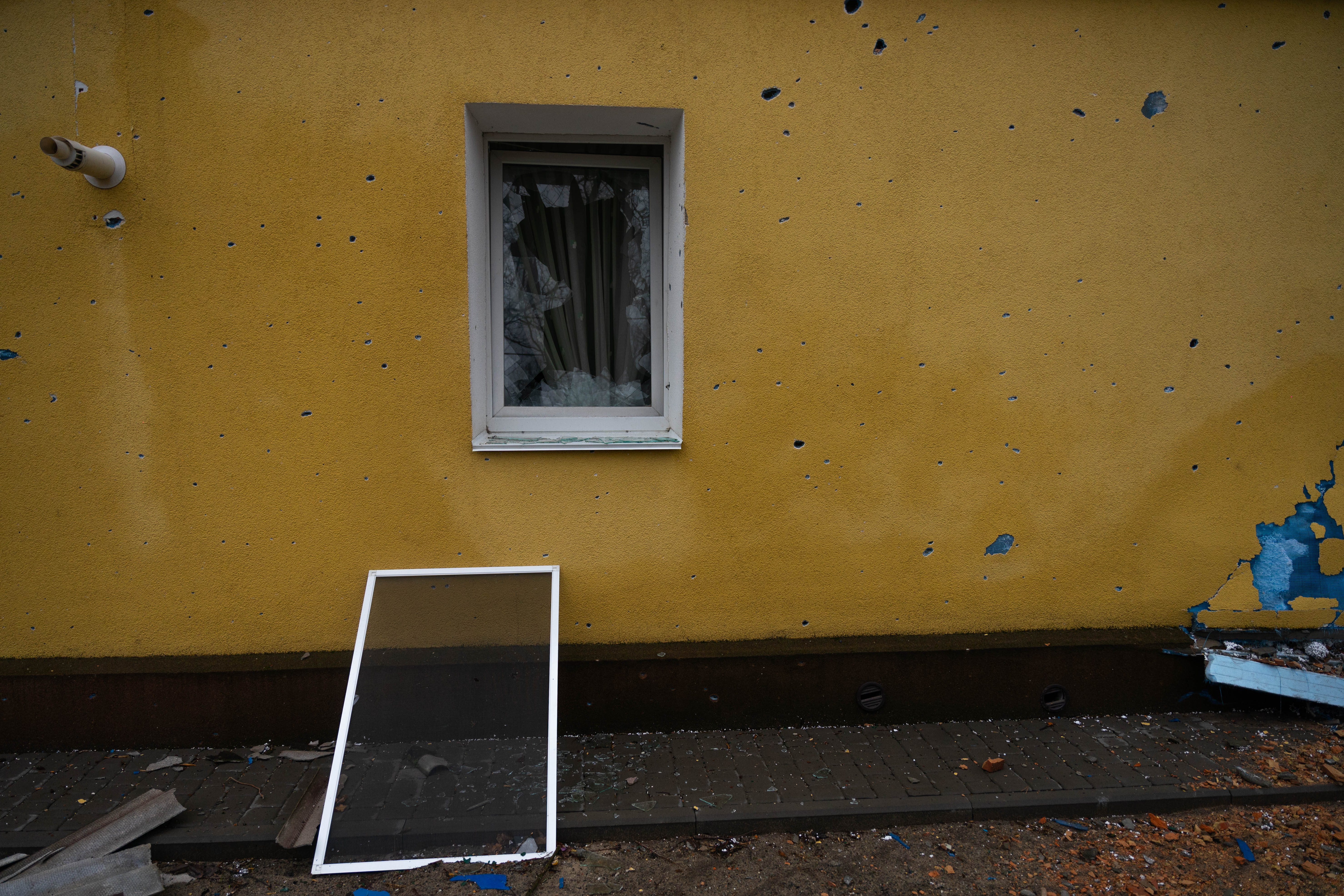 Metralla y ventanas rotas en la fachada de una casa frente a un parque de Irpin.