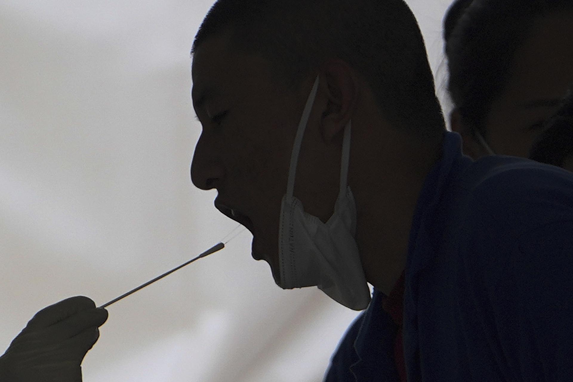 A worker has a throat swab sample taken at a coronavirus testing site set up near a commercial office complex.  (AP Photo/Andy Wong)
