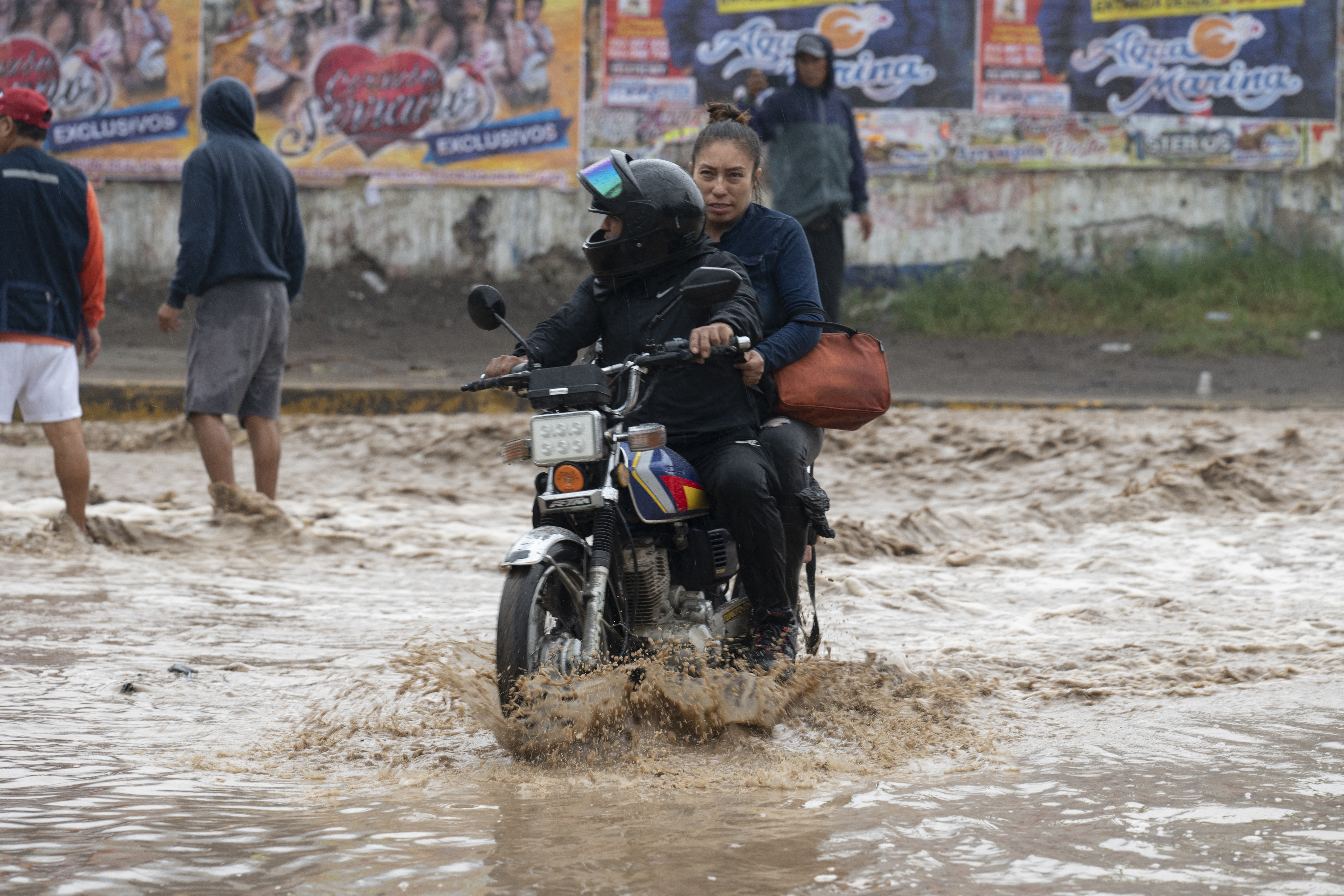En motos o a pie, los ciudadanos intentan cruzar de un tramo a otro en medio de las inundaciones causadas por los huaicos.(AFP)