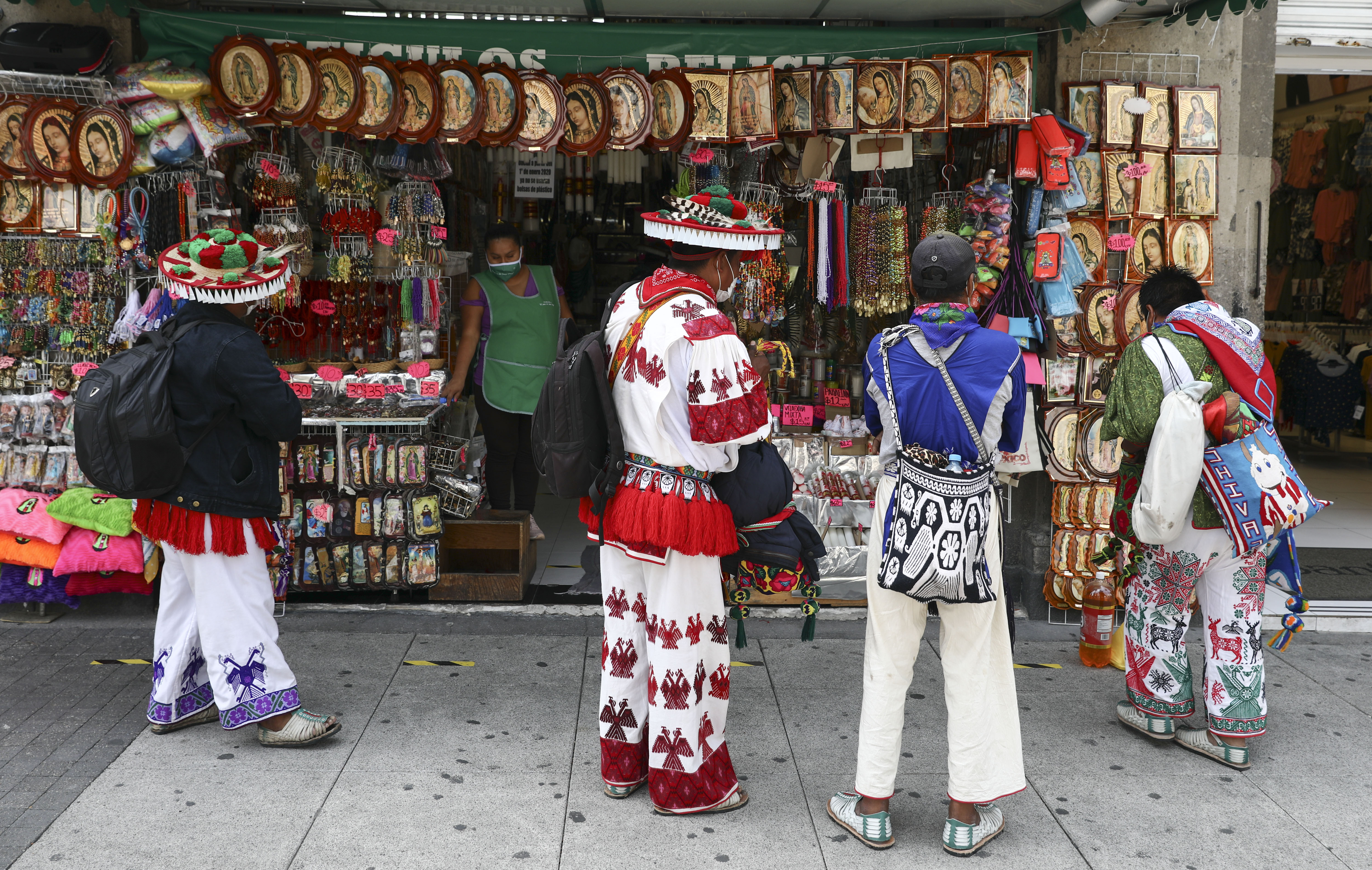 Los hombres indígenas huicholes observan imágenes religiosas a la venta fuera de la Basílica de Nuestra Señora de Guadalupe en la Ciudad de México, el lunes 29 de junio de 2020. (Foto: AP / Eduardo Verdugo)