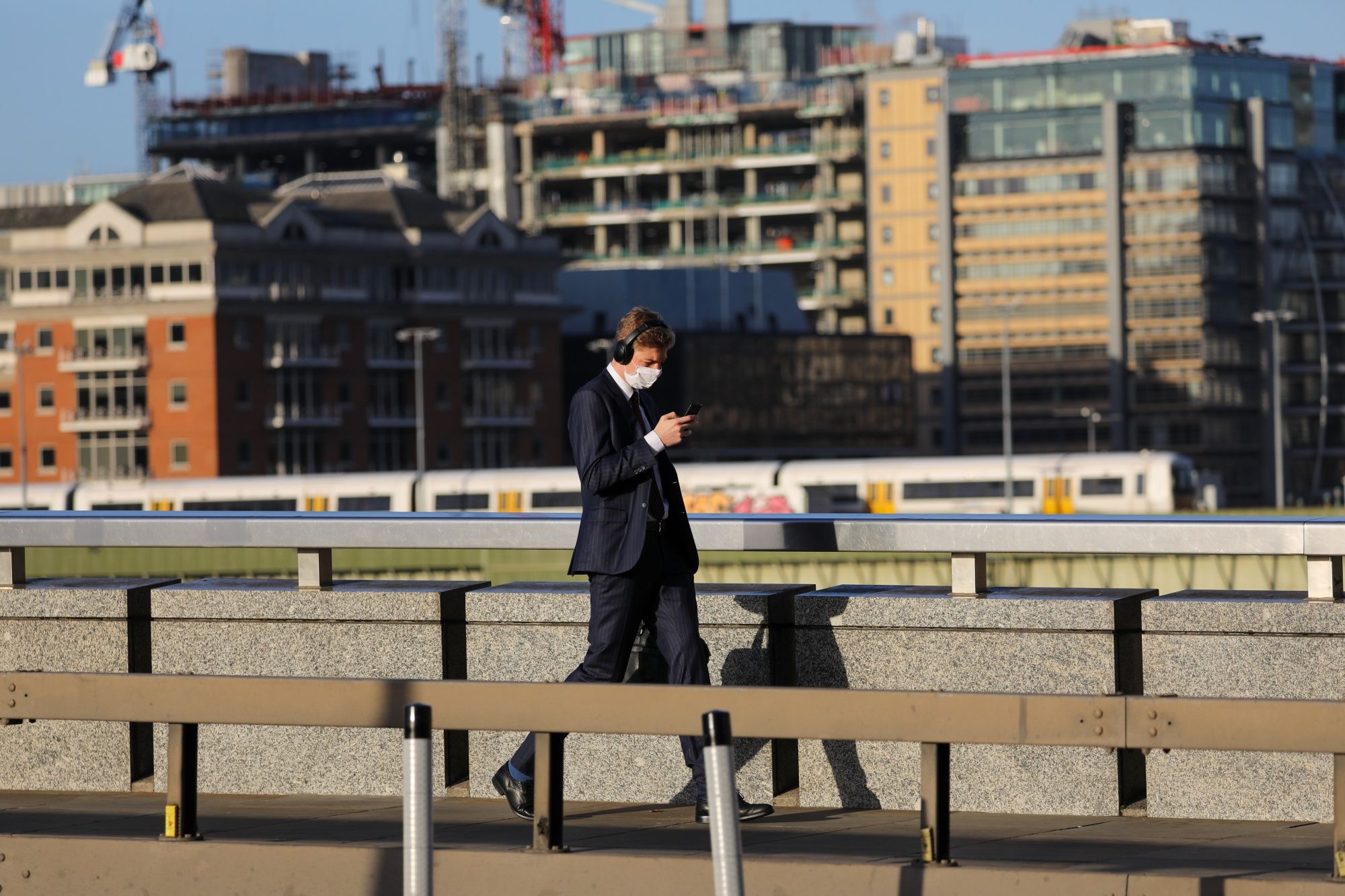A commuter, wearing a protective face mask, looks at his mobile phone as he crosses London Bridge in London, U.K., on Thursday, Oct. 15, 2020. London is on course for an imminent tightening of coronavirus restrictions, as cases continue to rise in Britain and its response fragments. Photographer: Simon Dawson/Bloomberg