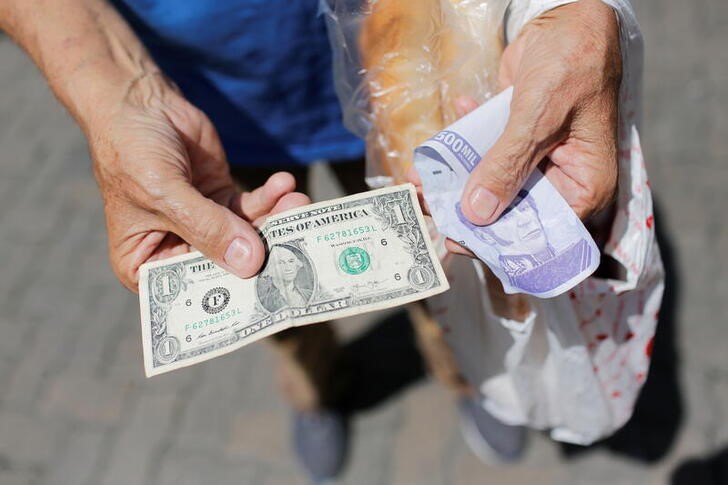 Un vendedor callejero sostiene un billete de un dólar junto a un billete de bolívares, en Caracas (REUTERS/Manaure Quintero/Archivo)