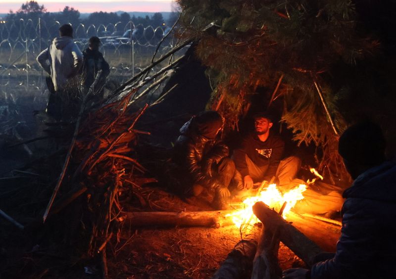 Varias personas se calientan junto a un fuego en un refugio improvisado junto a las concertinas de la frontera vallada de Bielorrusia con Polonia, en la región de Grodno, Bielorrusia, el 10 de noviembre de 2021. (Ramil Nasibulin/BelTA/Cedida a través de REUTERS)