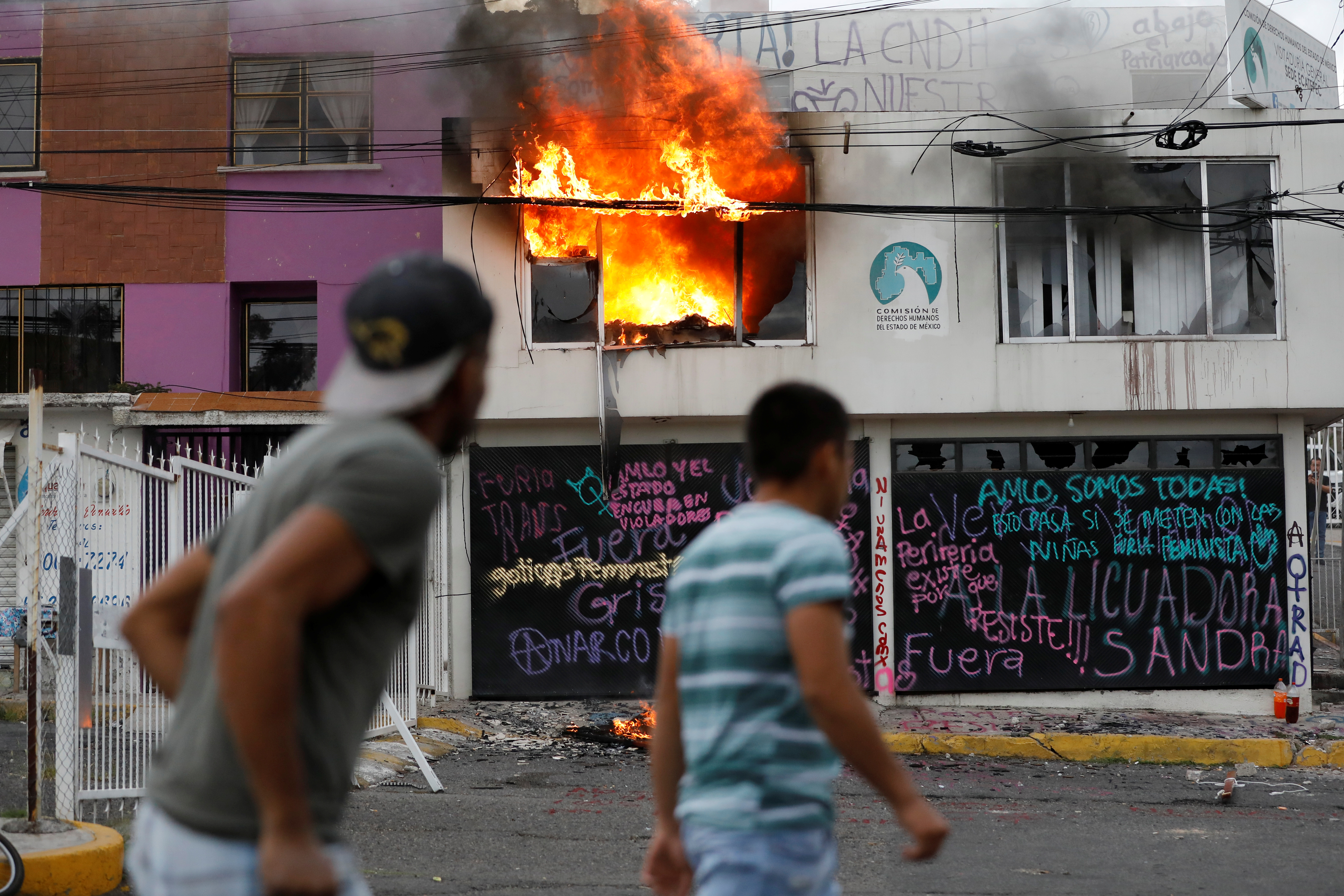 La gente observa un incendio que estalló luego de que miembros de un colectivo feminista destrozaran las instalaciones de la comisión de derechos humanos del estado de México, en apoyo a víctimas de violencia de género, en Ecatepec, Estado de México, México el 11 de septiembre de 2020.