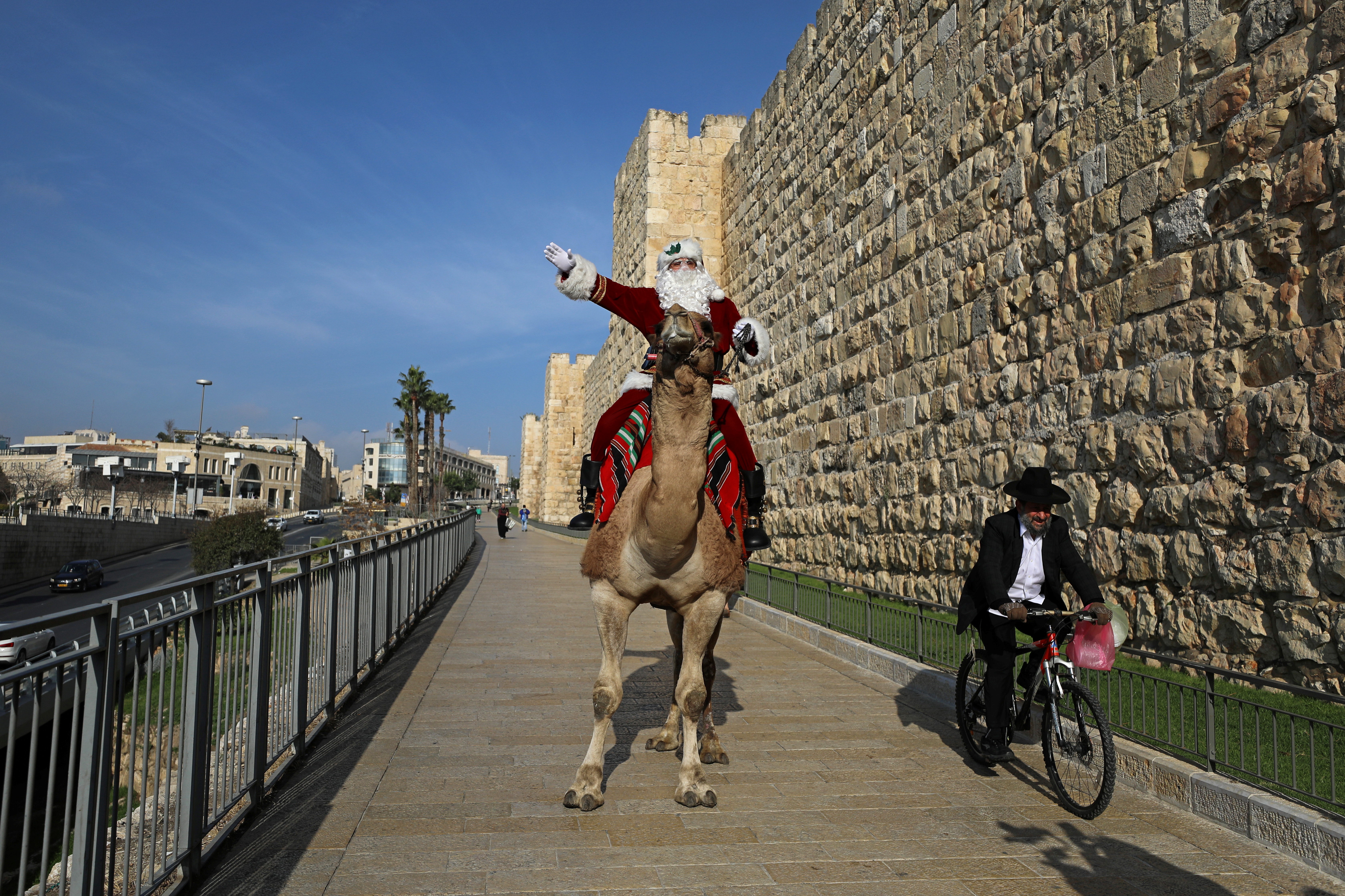 Un hombre judío ultraortodoxo pasa en bicicleta por delante de Issa Kassissieh disfrazado de Papá Noel después de repartir árboles de Navidad en las afueras de la Ciudad Vieja de Jerusalén  (REUTERS/Ammar Awad)