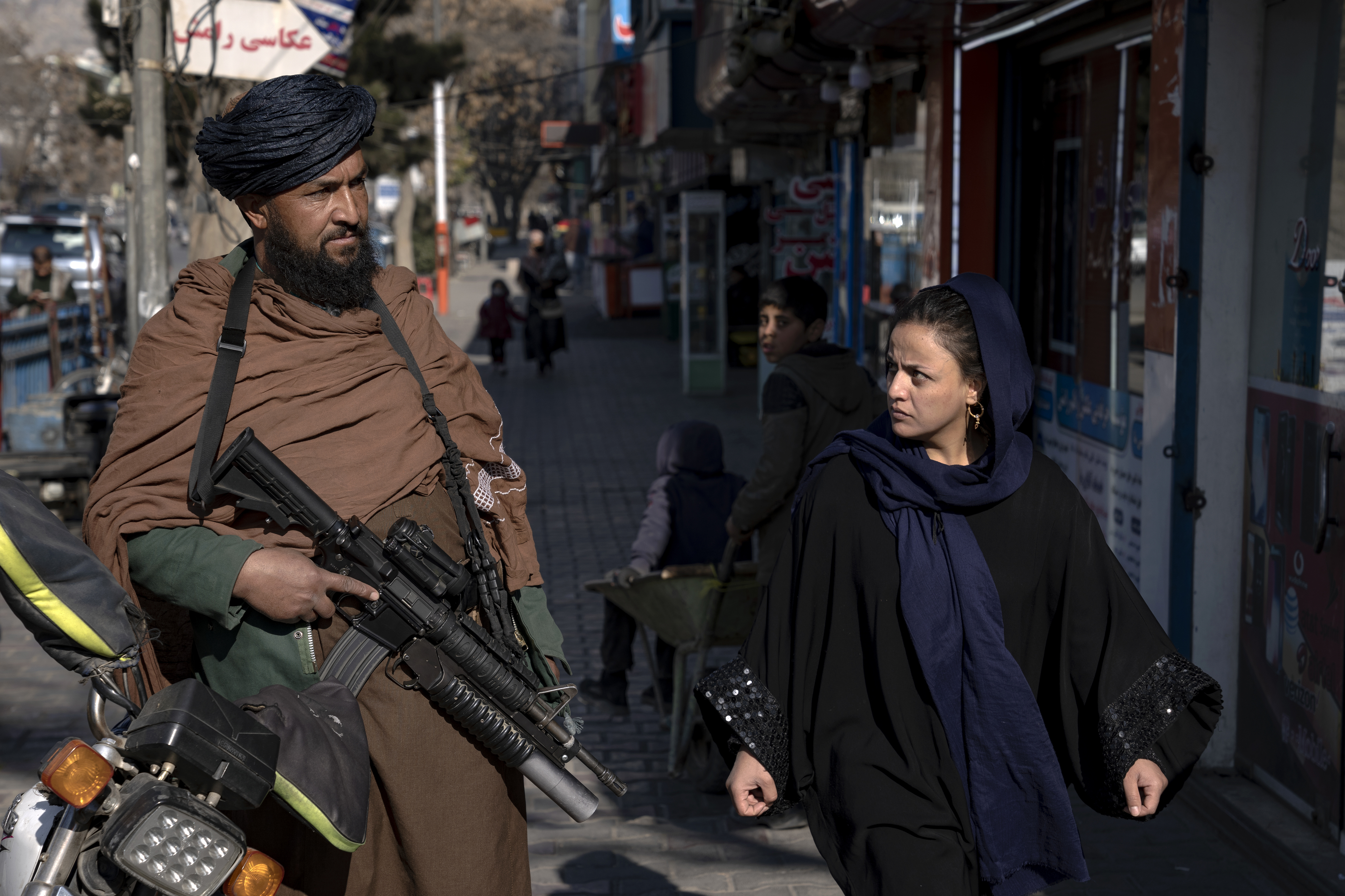 Un combatiente talibán patrulla mientras una mujer pasa a su lado en una calle de Kabul, Afganistán
