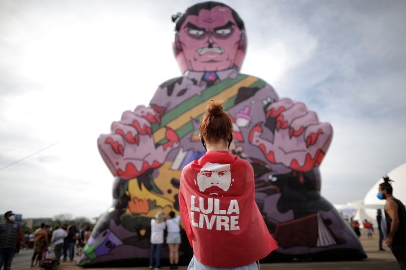 Una manifestante, tapada con una imagen del expresidente de Brasil Luiz Inacio Lula da Silva, toma una foto de un muñeco inflable conocido como "Pixuleco" que representa al presidente Jair Bolsonaro durante una protesta contra el presidente en Brasilia (Foto: REUTERS/Ueslei Marcelino)