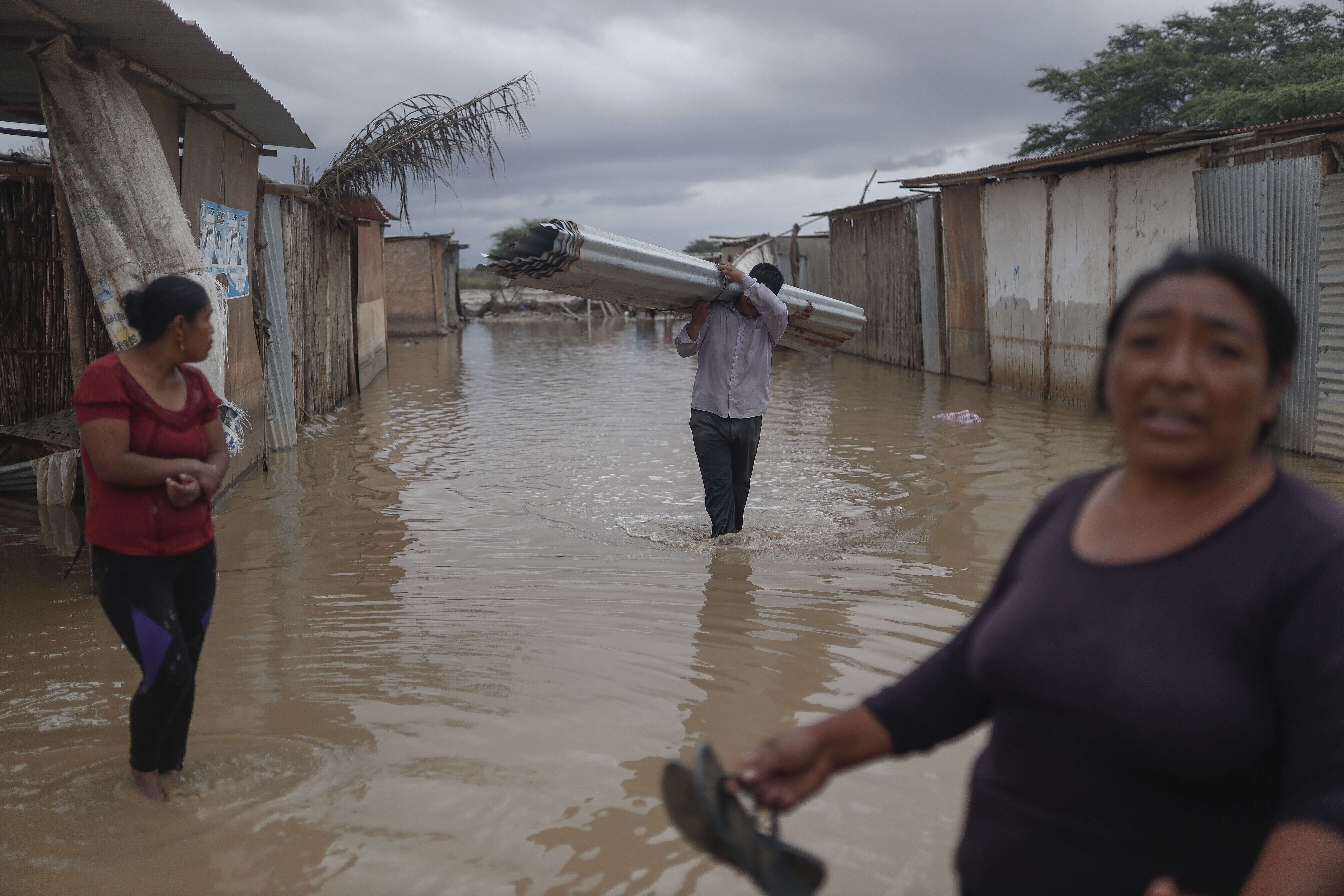 Un residente lleva material corrugado a través de una calle inundada por las fuertes lluvias del ciclón Yaku en Chiclayo, Perú, el domingo 12 de marzo de 2023. (AP Foto/Aldair Mejía)