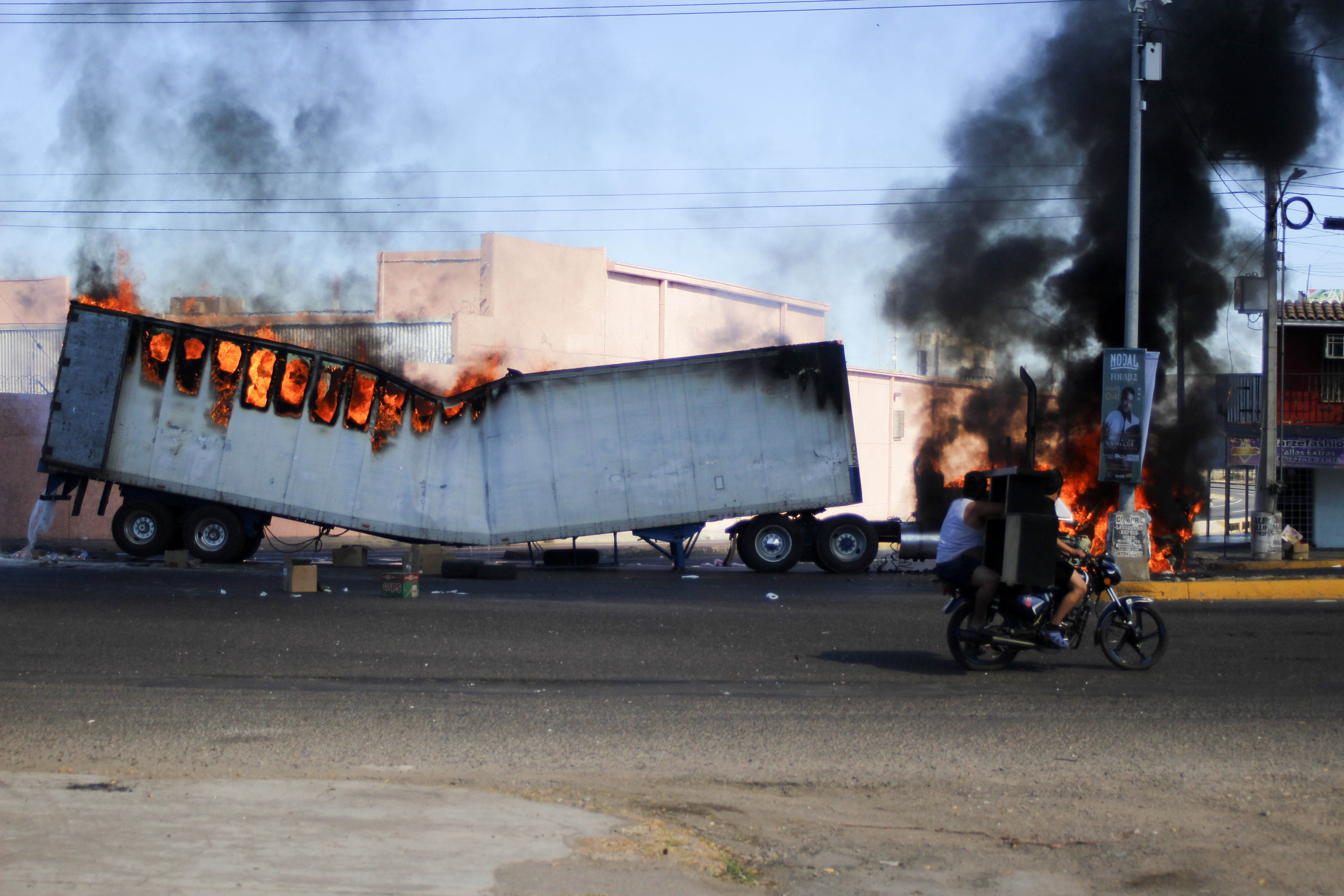 Dos hombres a bordo de una motocicleta pasan junto a un camión en llamas en las calles de Culiacán, en el estado de Sinaloa, el 5 de enero de 2023. (AP Foto/Martín Urista)