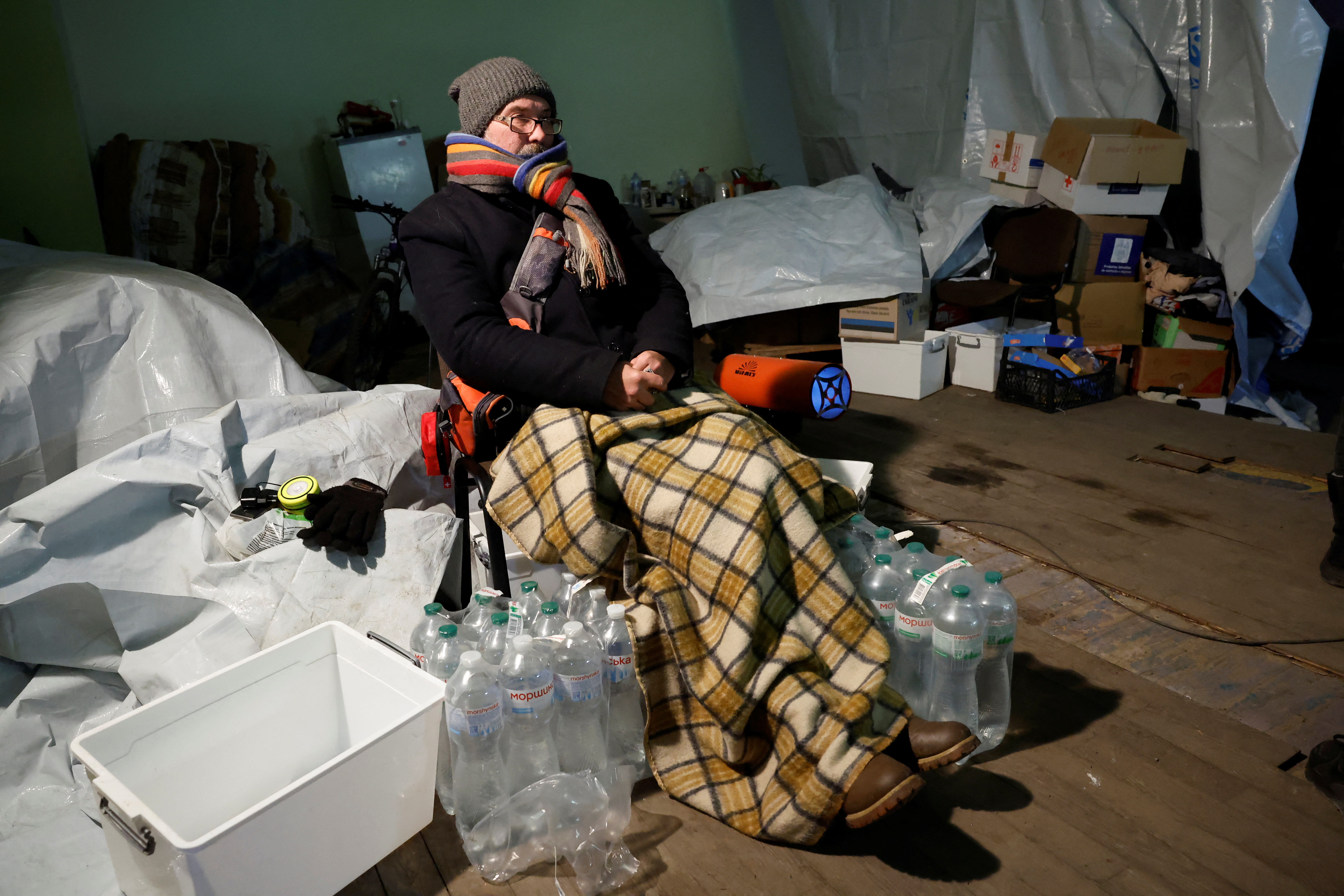 A man warms himself with blankets in a shelter, in Bakhmut