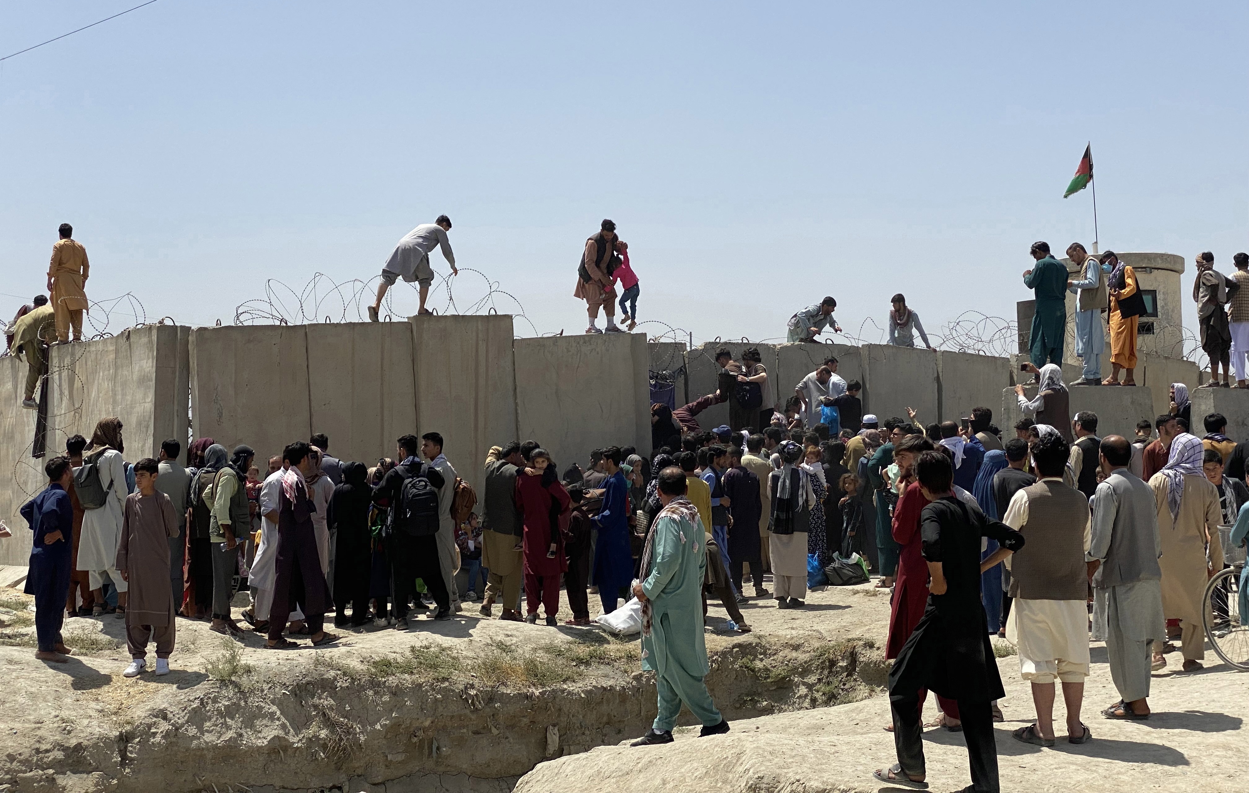 Afganos se agolpan a lo largo del muro del aeropuerto internacional Hamid Karzai antes de saltarlo en un intento de abandonar el país, este lunes en Kabul, después de darse a conocer de que el propio presidente afgano, Ashra Ghani, huyera en secreto. EFE/STRINGER
