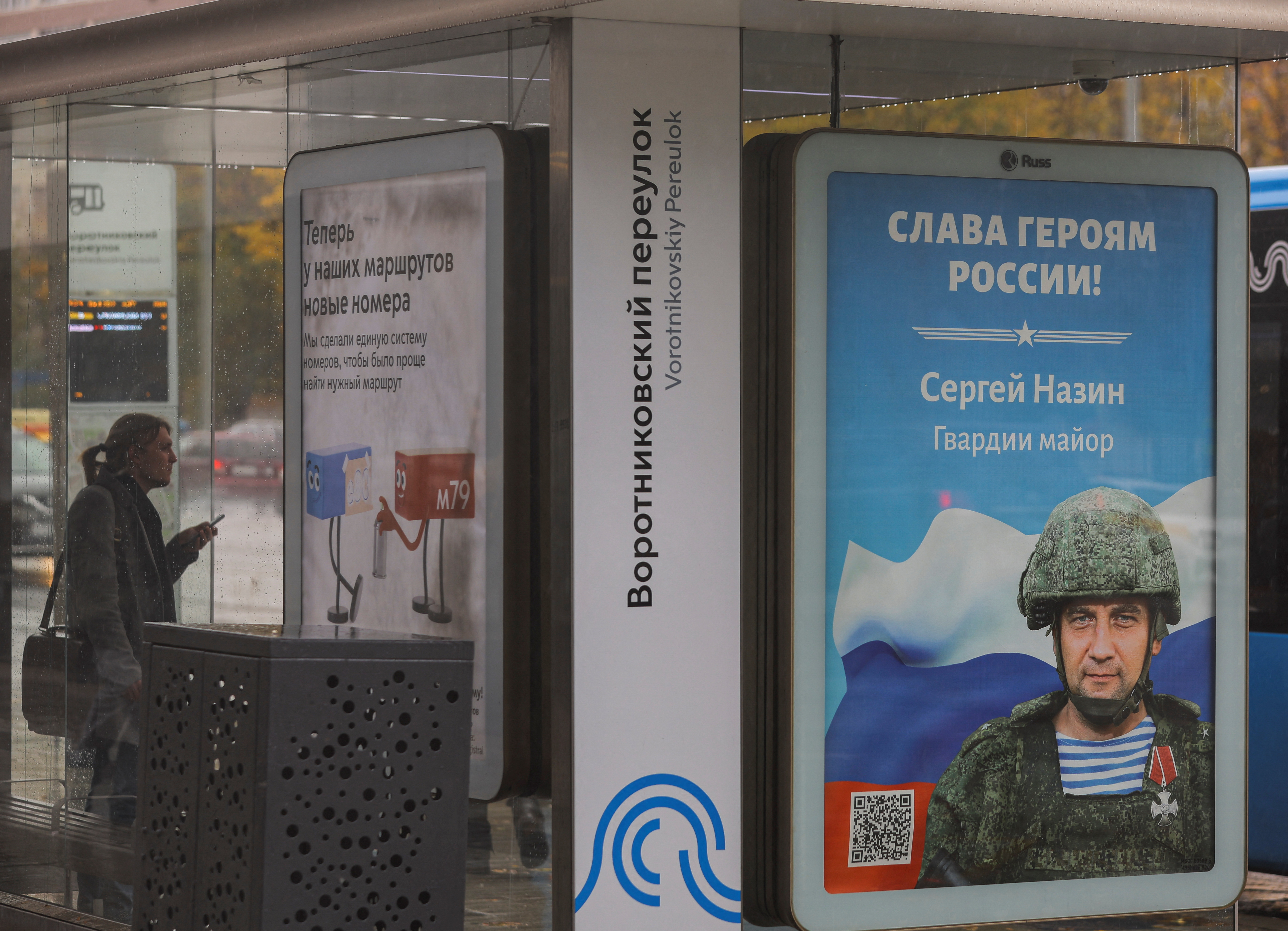 Una persona espera un autobús en Moscú mientras puede verse una imagen de un soldado ruso con el eslogan "Gloria a los héroes de Rusia". La guerra comienza a sentirse en las calles de la capital rusa (Reuters)