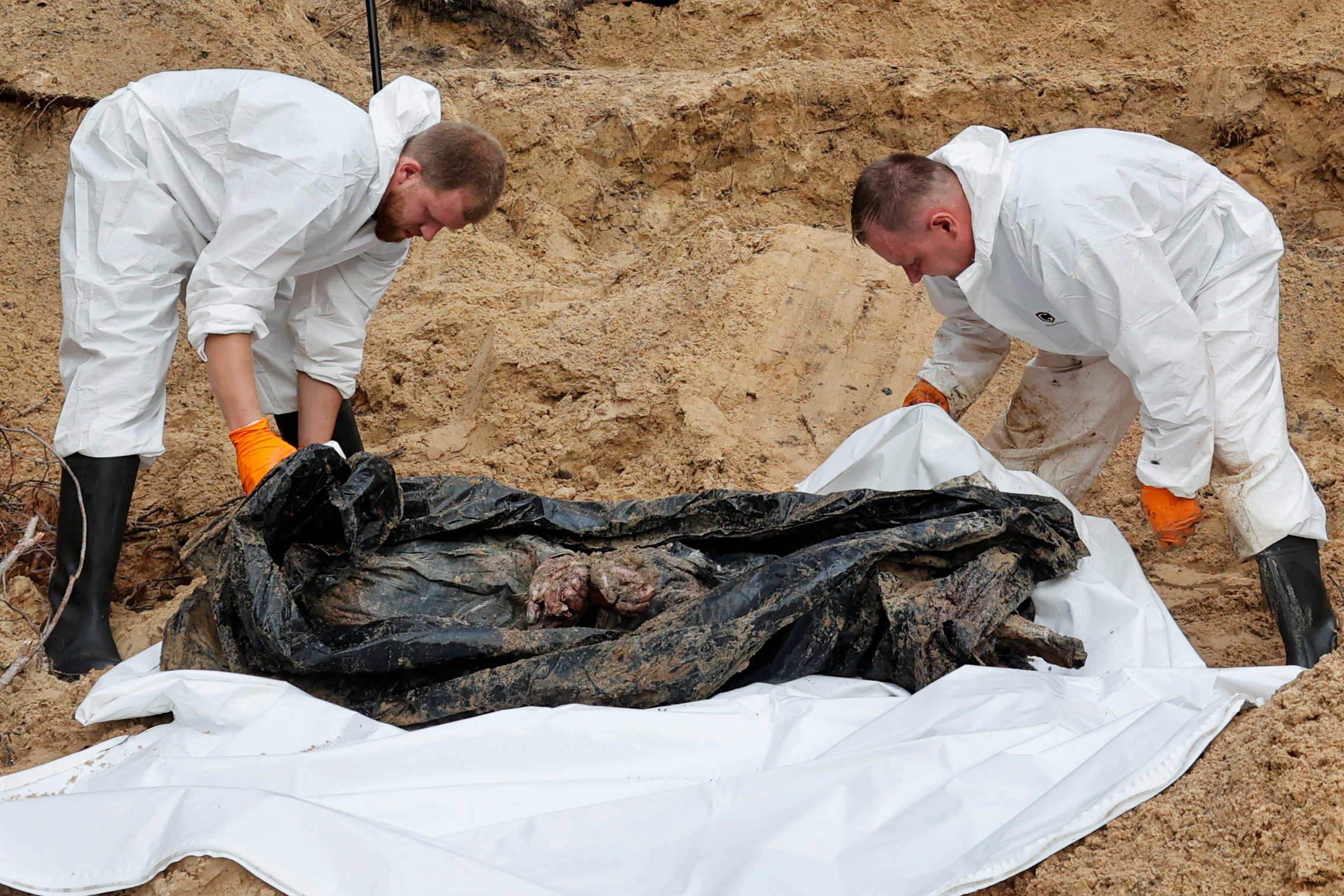 Los técnicos forenses exhuman el cuerpo de un soldado ucraniano con las manos atadas a la espalda de una fosa común en el lugar de un cementerio improvisado en la ciudad de Izyum (REUTERS)