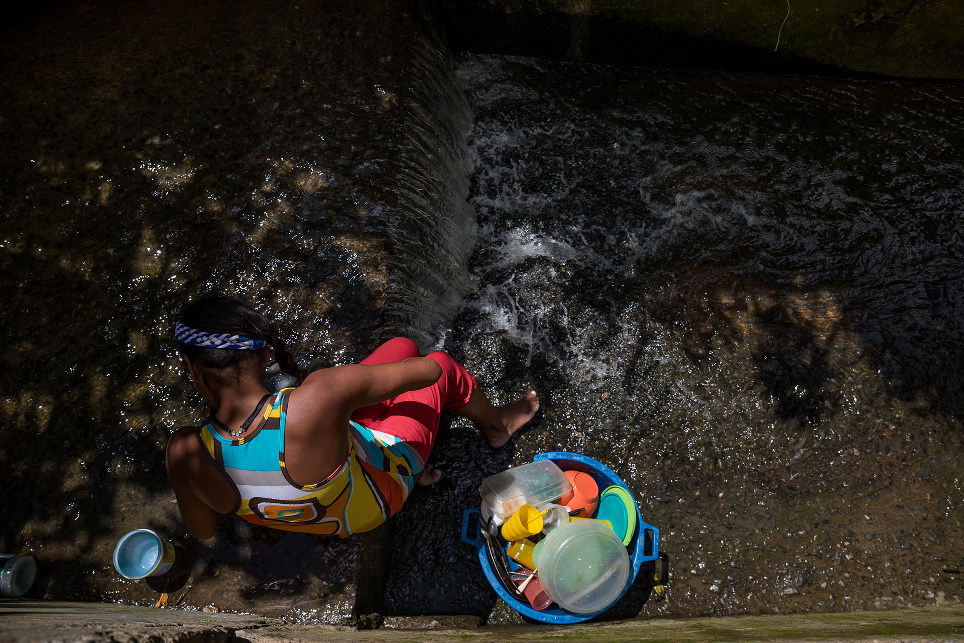 Una mujer lavando utensilios de cocina en una quebrada de agua, en Caracas (EFE/ Miguel Gutiérrez)