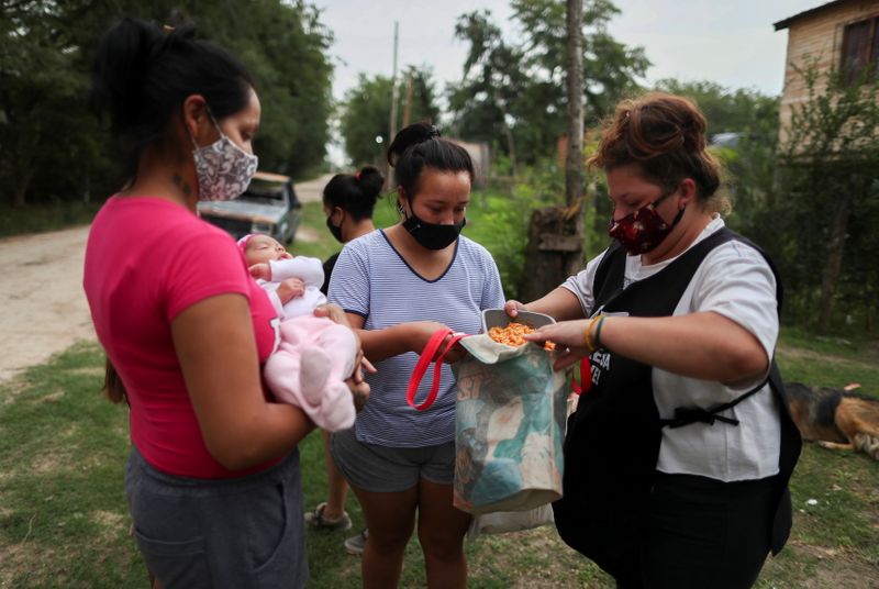 Voluntaria entrega una ración de guiso a personas de escasos recursos en un recipiente de plástico en un comedor social organizado en la casa de Aida Mariela Unayche, en Manzanares (REUTERS/Agustin Marcarian)