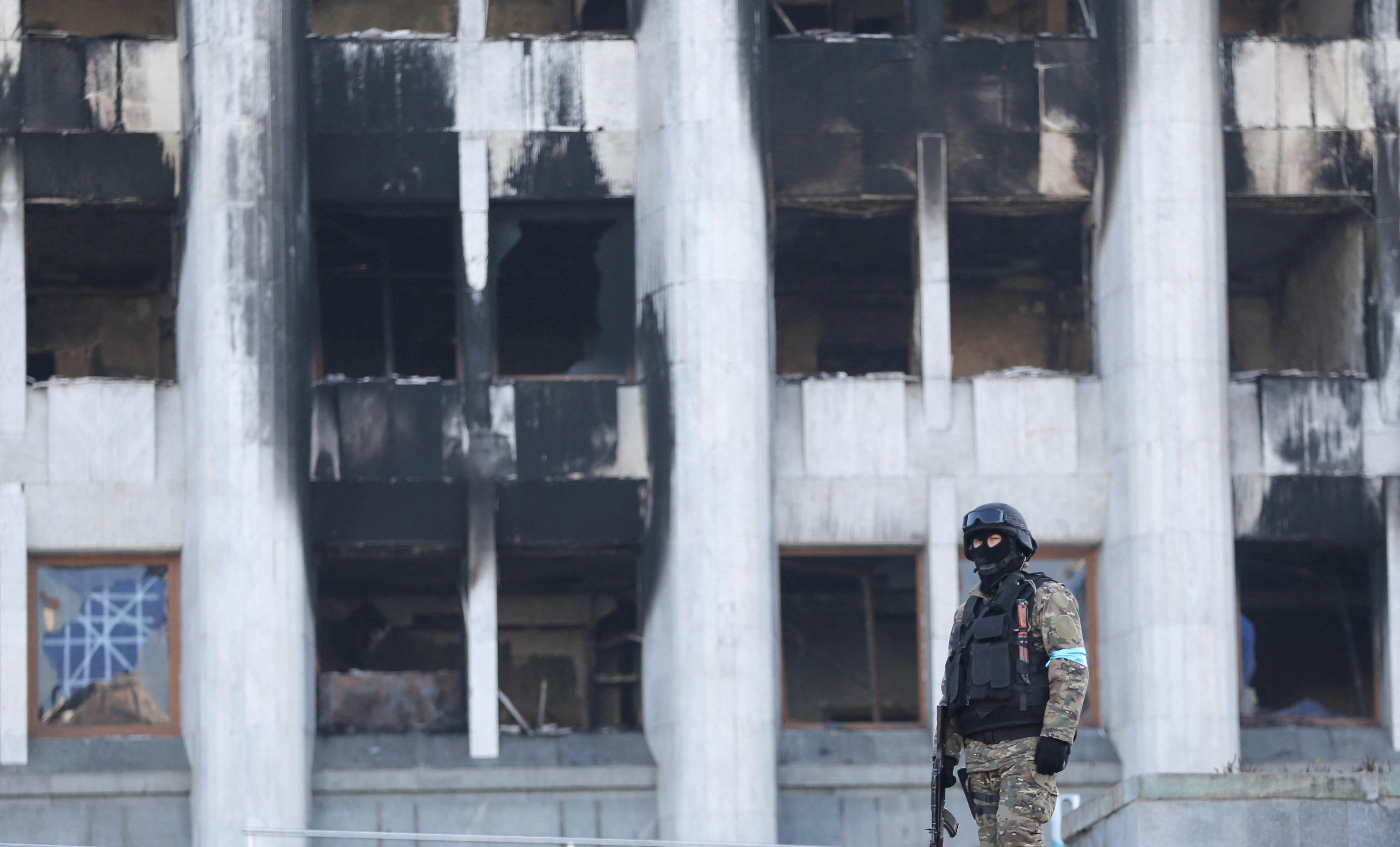 A Kazakh service member stands guard outside the city administration headquarters, which was set on fire during recent protests triggered by fuel price increase, in Almaty, Kazakhstan January 12, 2022. REUTERS/Pavel Mikheyev