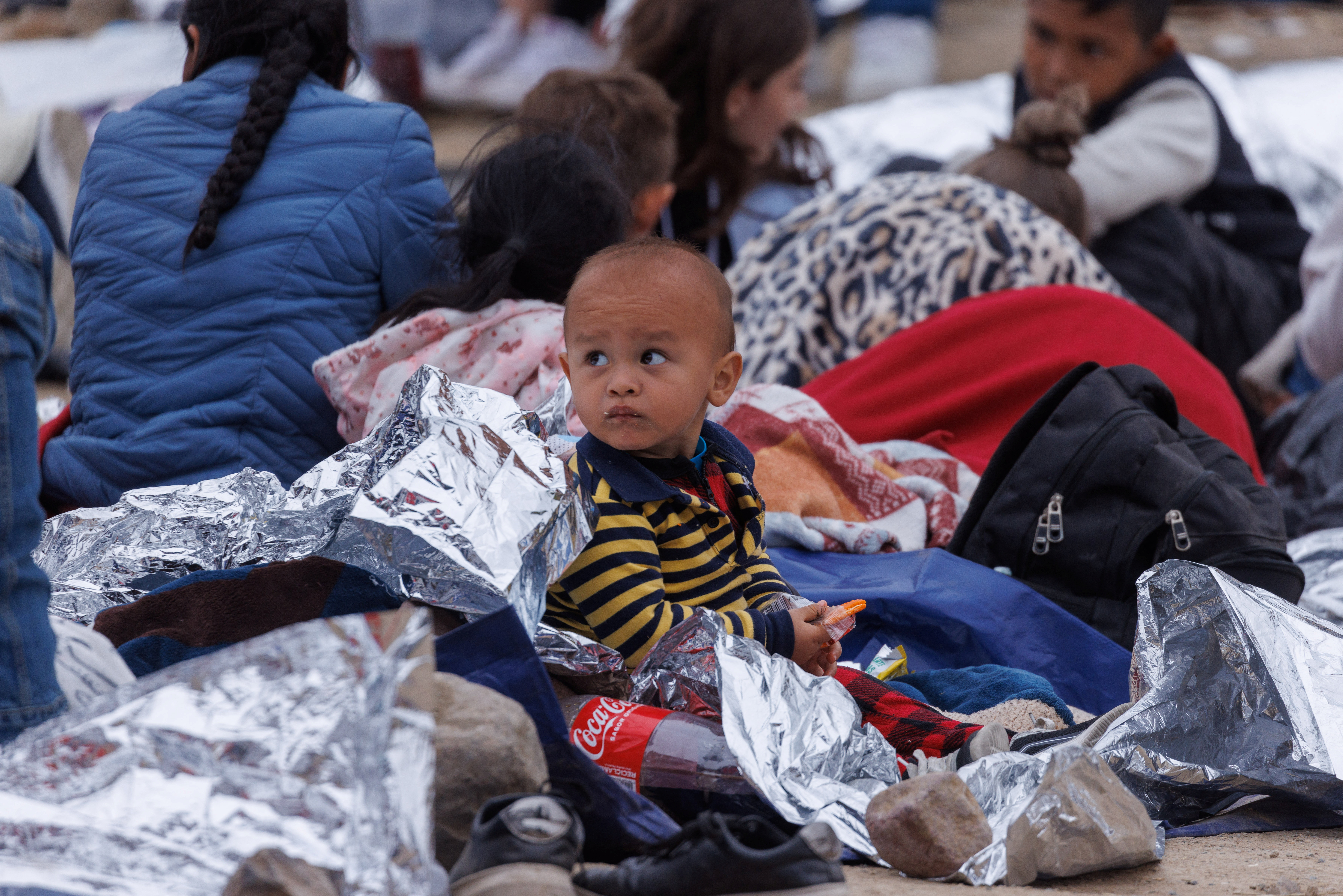 Un niño come una galleta mientras los migrantes se reúnen entre las vallas fronterizas primaria y secundaria entre Estados Unidos y México (REUTERS/Mike Blake)