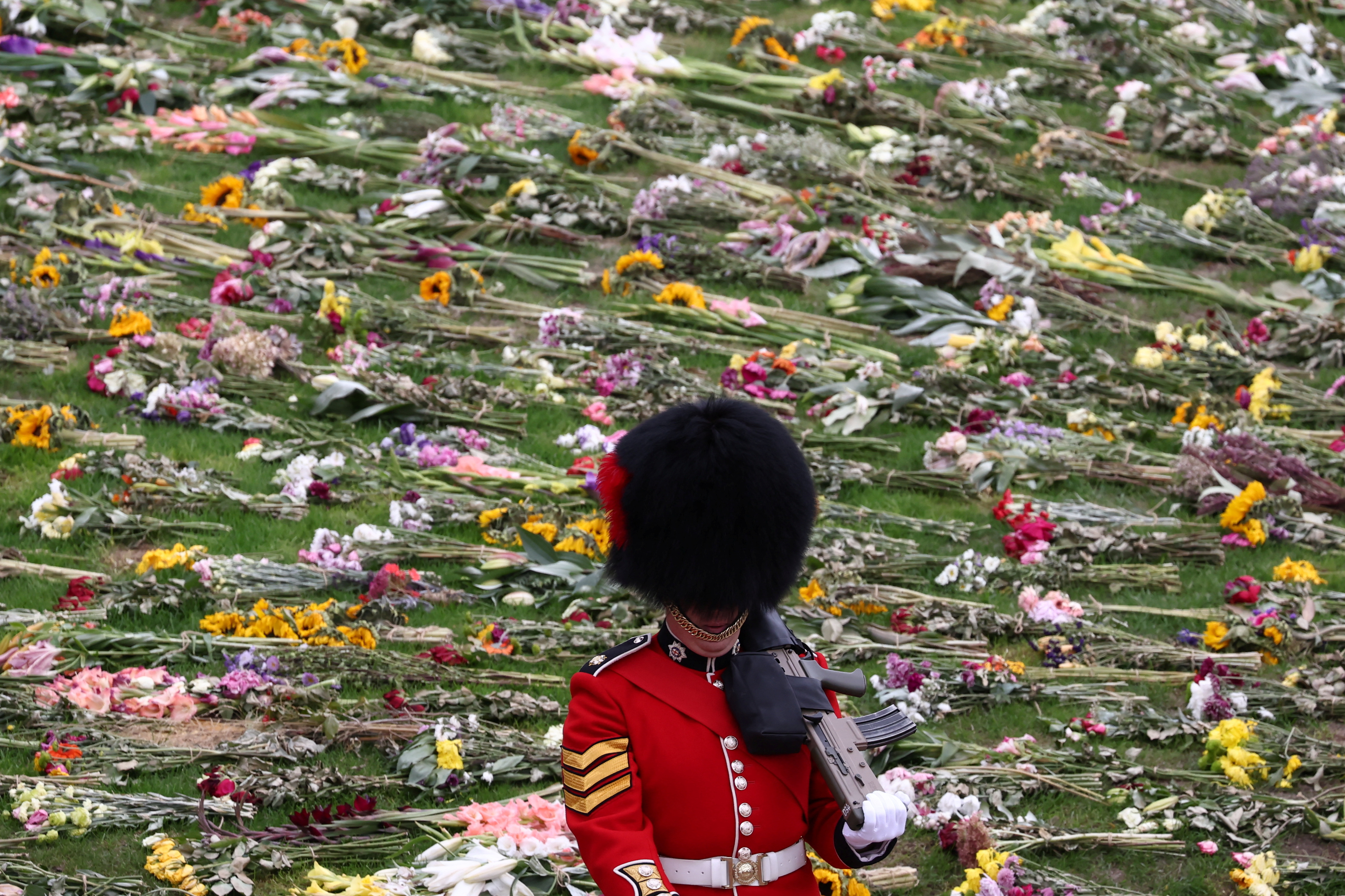 Una Guardia Real hace guardia en el Castillo de Windsor en Windsor se encuentra al lado de un campo lleno de flores. 