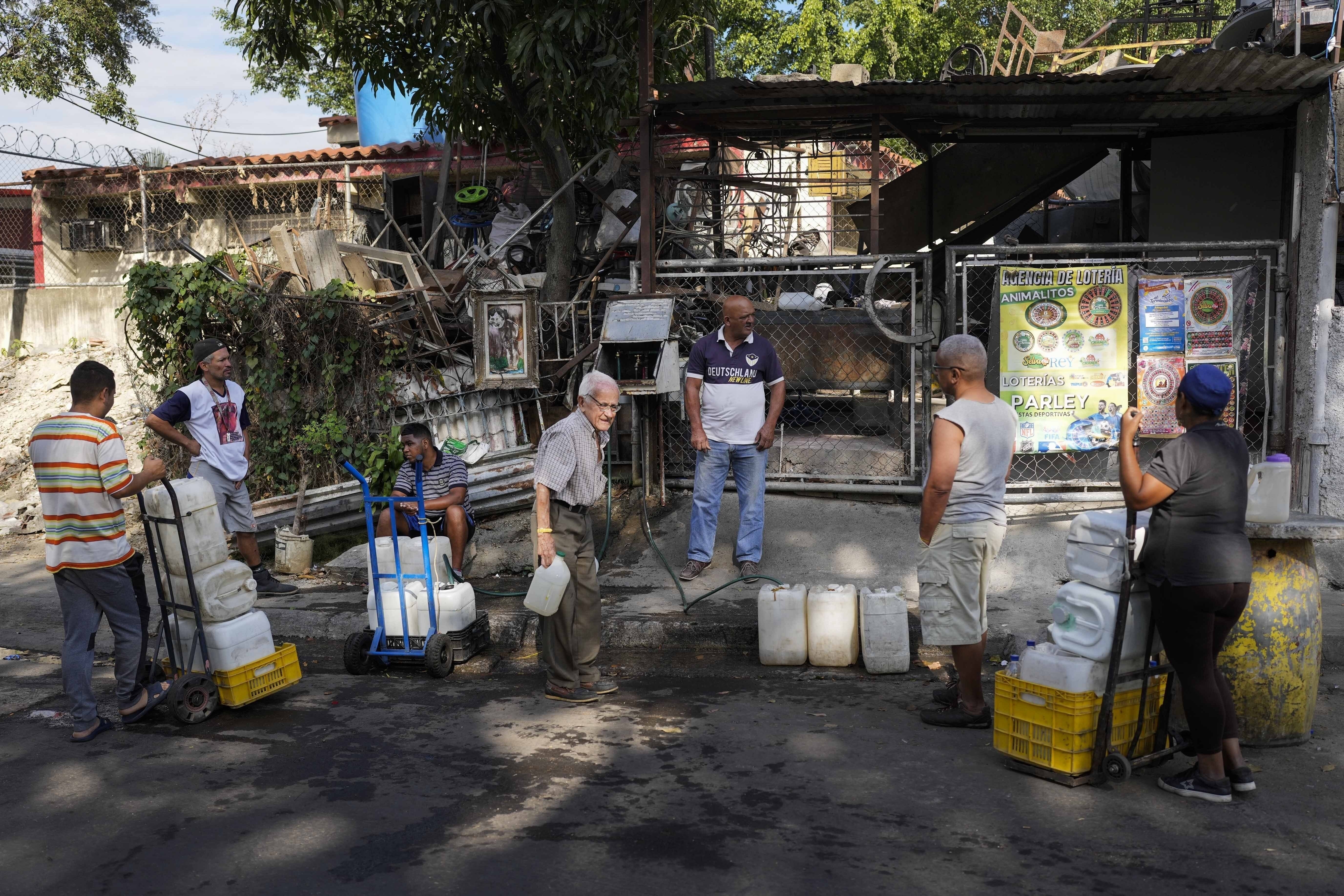 Residentes esperan su turno para llenar sus recipientes con el agua recolectada en un túnel de autopista abandonado, en el barrio de Cotiza, Caracas, Venezuela, el 20 de marzo de 2023. (AP Foto/Matías Delacroix)