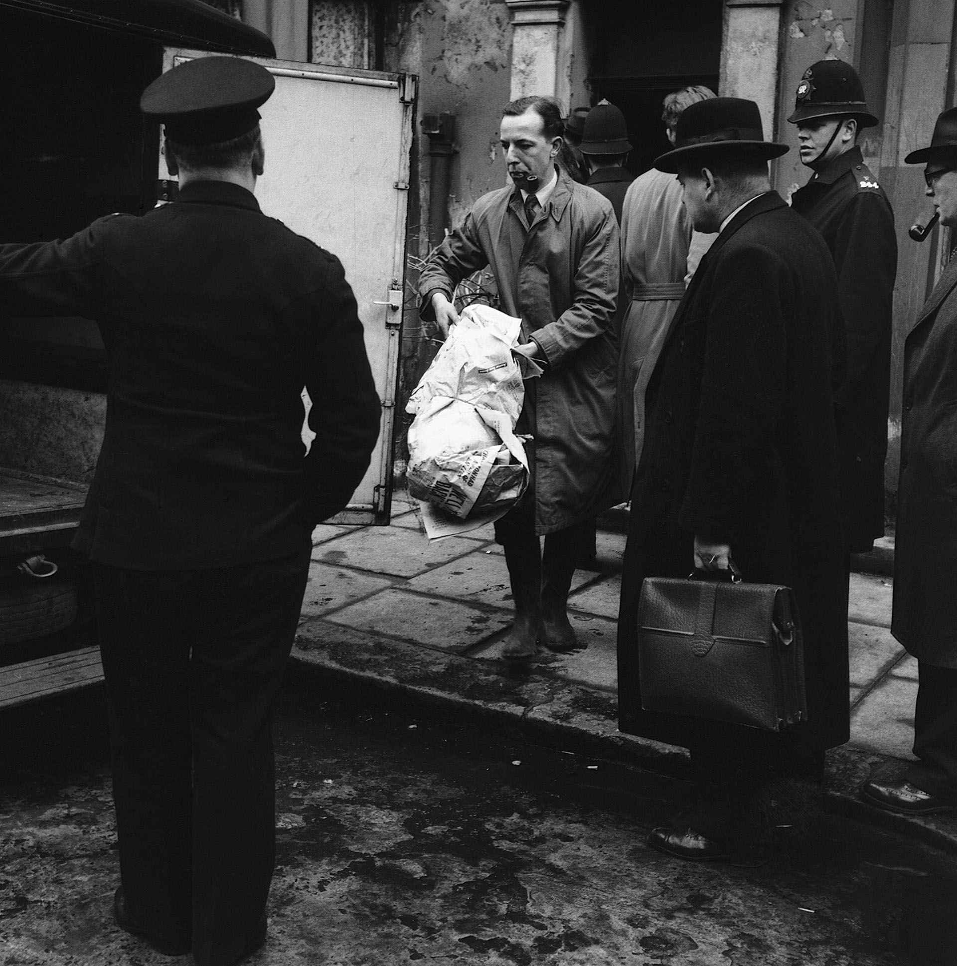 Un oficial de policía lleva varios huesos envueltos en periódicos hasta una furgoneta de policía que espera fuera del número 10 de Rillington Place, Londres. Los restos eran los de la quinta persona asesinada por el John Reginald Christie (Hulton-Deutsch Collection/CORBIS/Corbis vía Getty Images)

