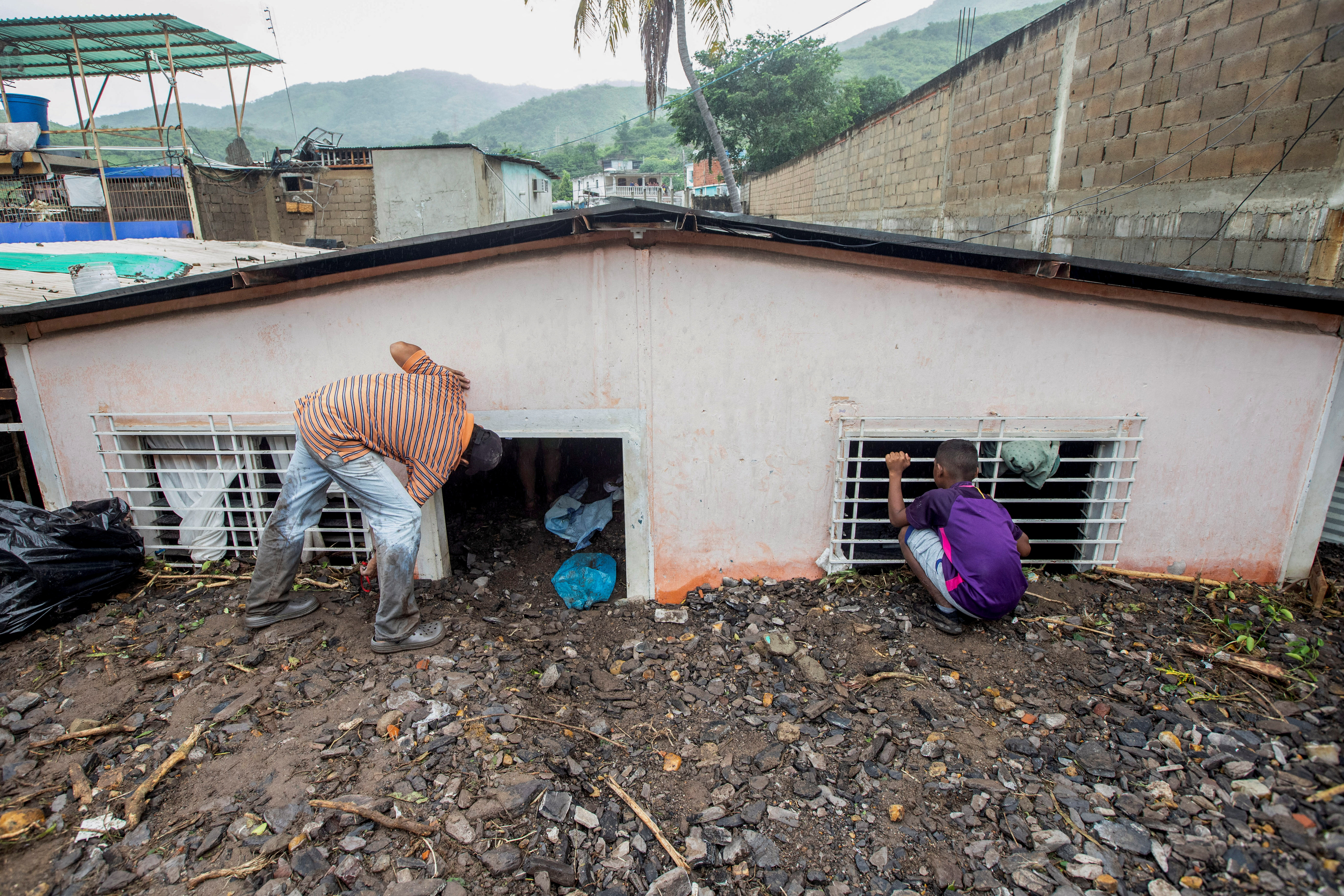 Los residentes miran dentro de una casa dañada después de las inundaciones causadas por las fuertes lluvias, en Puerto la Cruz