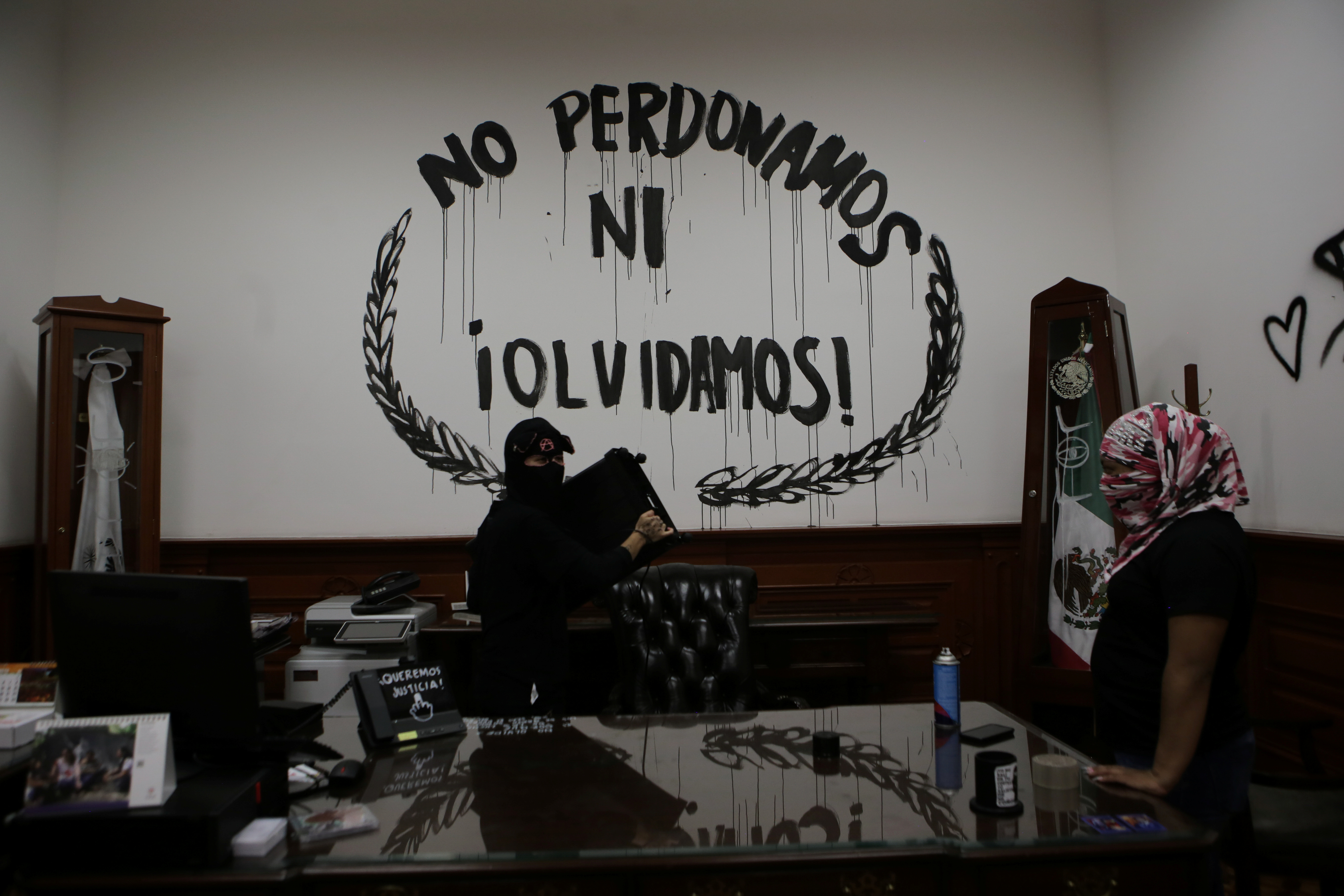 Una integrante de un colectivo feminista carga un bote de basura junto a un grafiti que dice