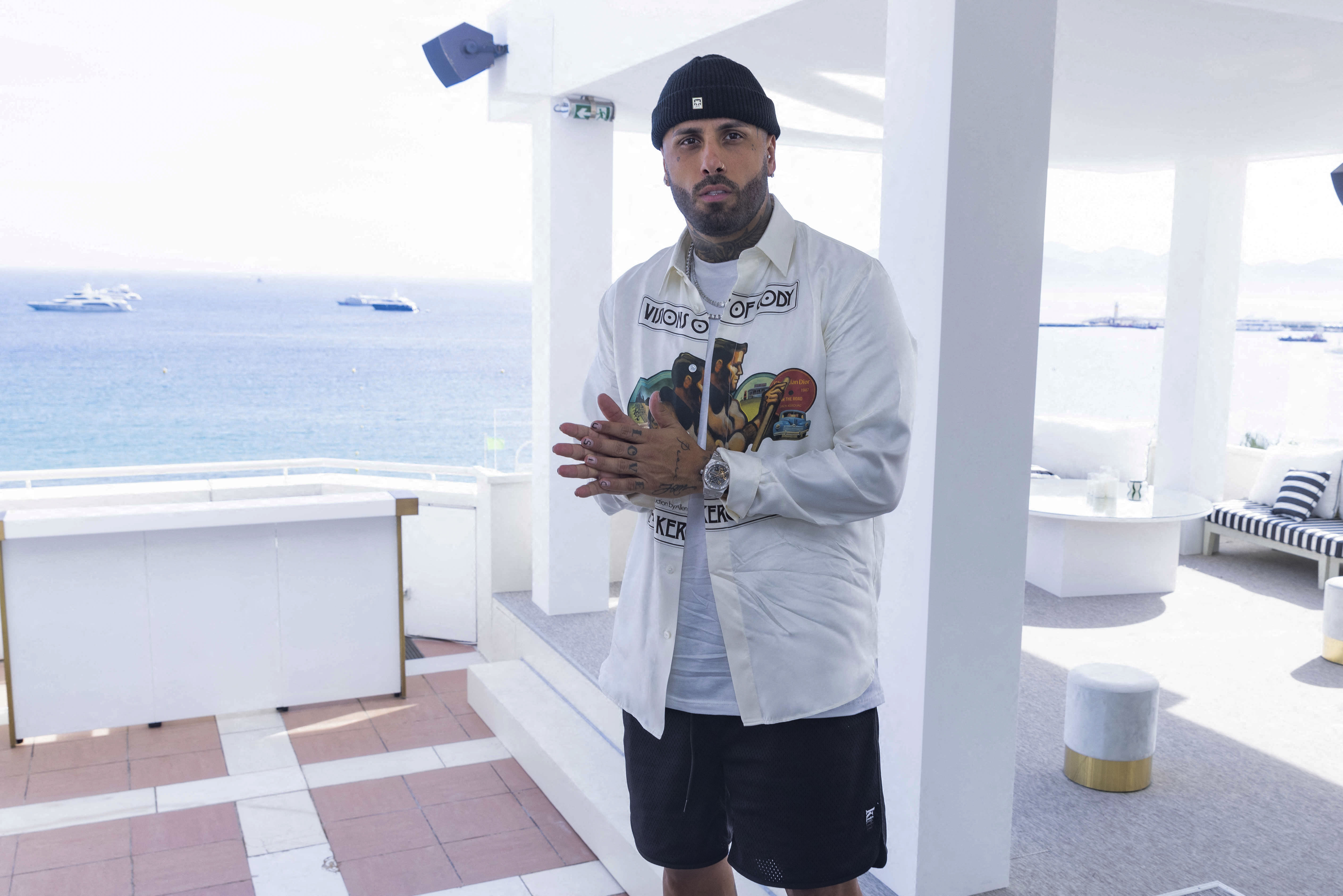 Nicky Jam posed for the photographers from the terrace of the exclusive hotel where he is staying to attend the 75th edition of the Cannes International Film Festival.  The musician wore a printed shirt with a classic white shirt, and black shorts that he combined with his wool hat