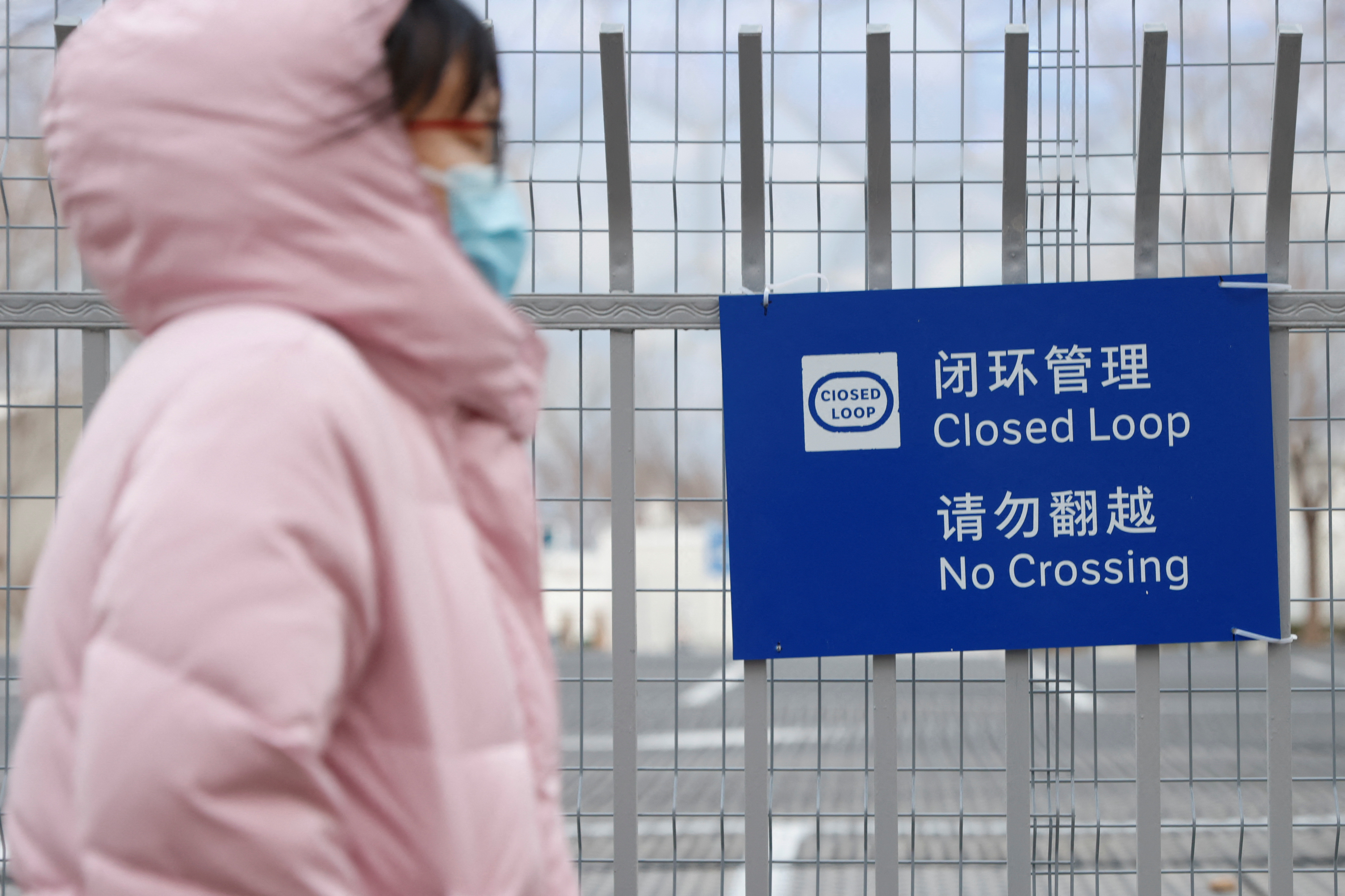 A woman walk pasts a sign on a fence marking the limit of the closed loop "bubble" area created to prevent the spread of coronavirus disease (COVID-19) during the upcoming Beijing 2022 Winter Olympics, in Beijing, China January 19, 2022. REUTERS/Carlos Garcia Rawlins